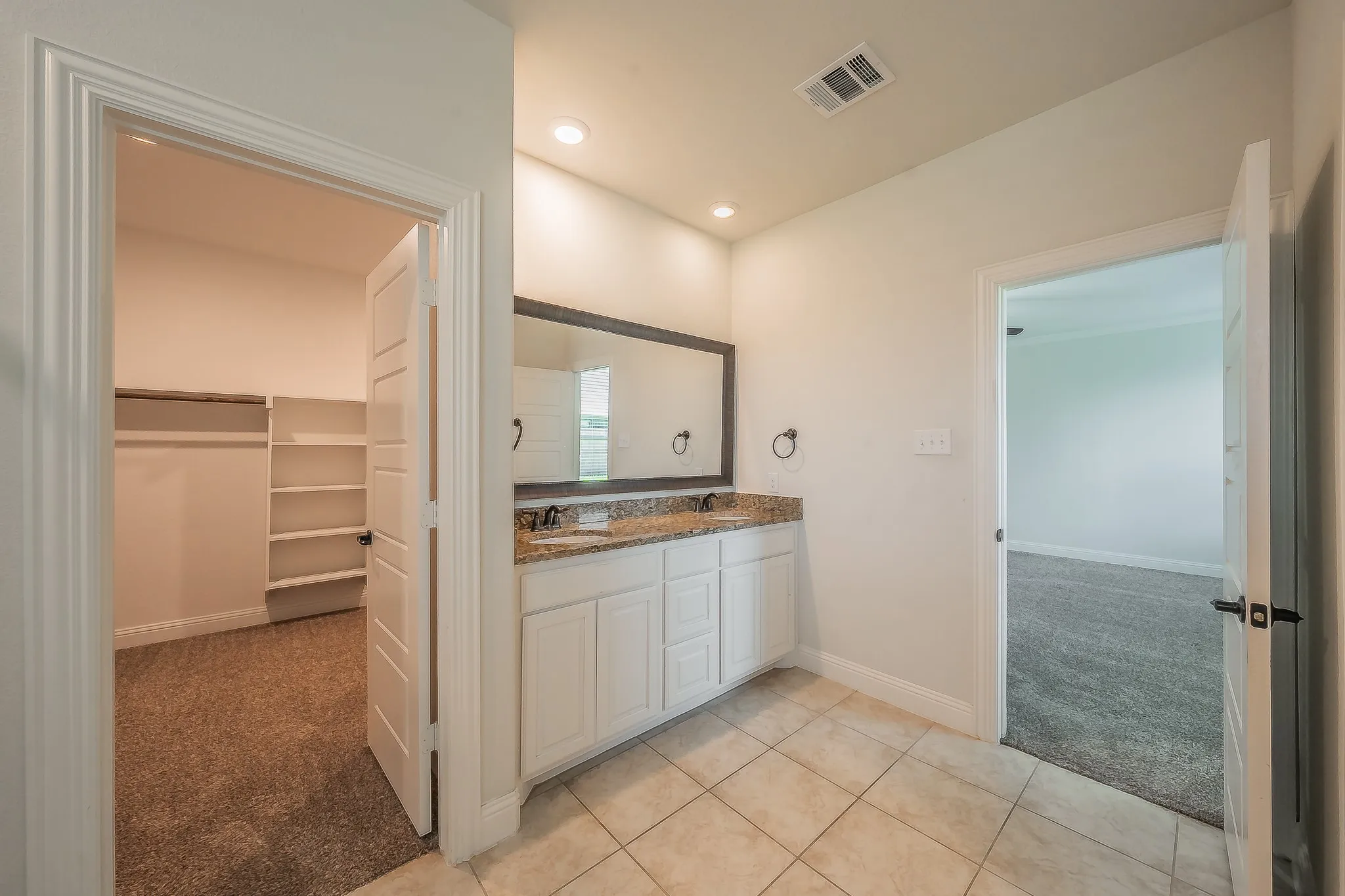 Bathroom vanity featuring a light-colored granite countertop, dual sinks, and a large framed mirror
