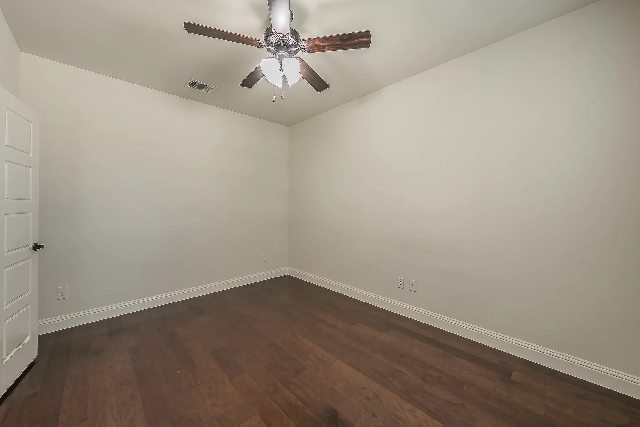 Room featuring wood-finish flooring, white baseboards, light-toned walls, a four-panel interior door with dark hardware, and a ceiling fan with integrated lighting