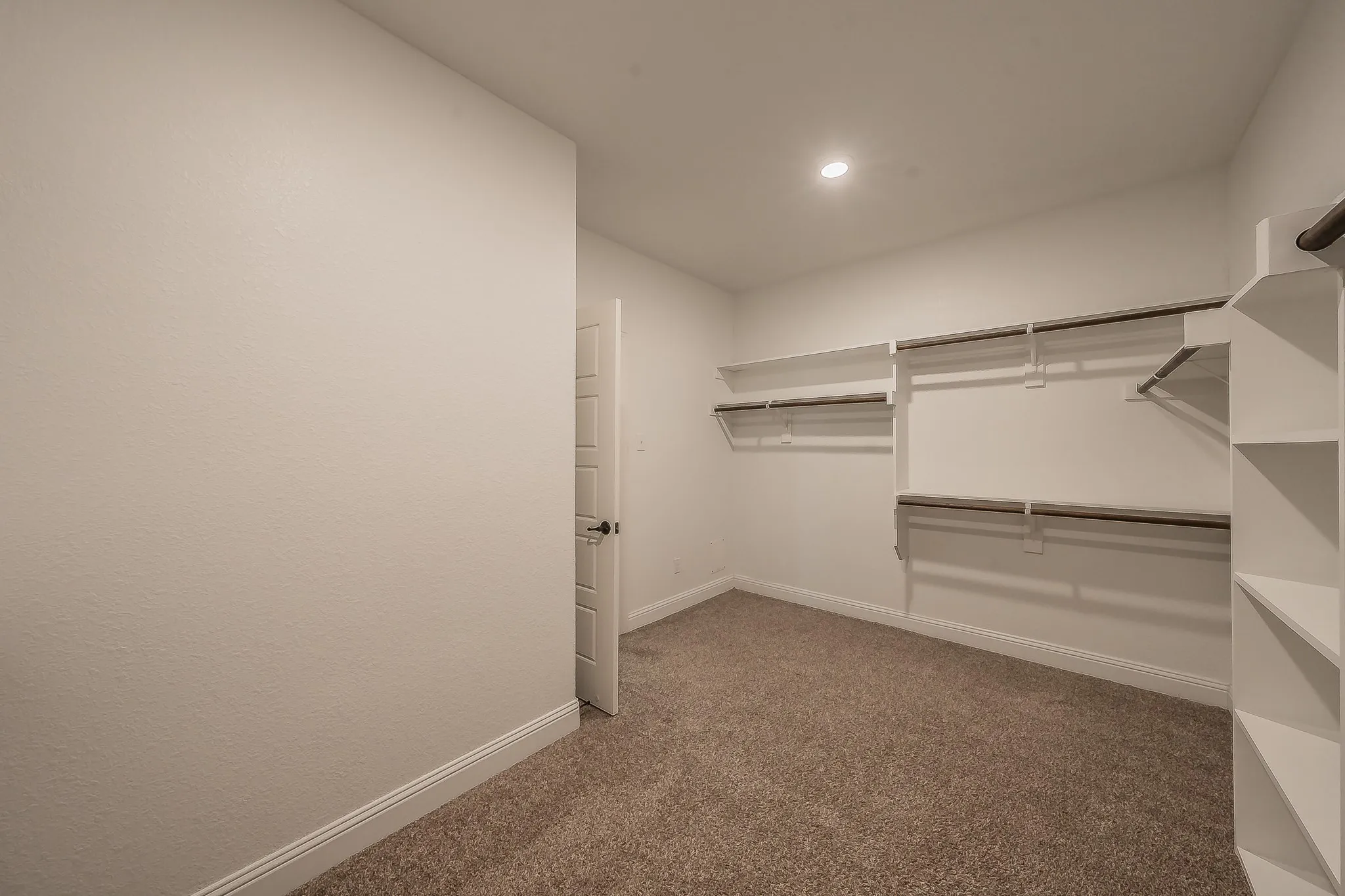 Walk-in closet featuring built-in shelving, multiple hanging rods, recessed ceiling lighting, and neutral carpeting