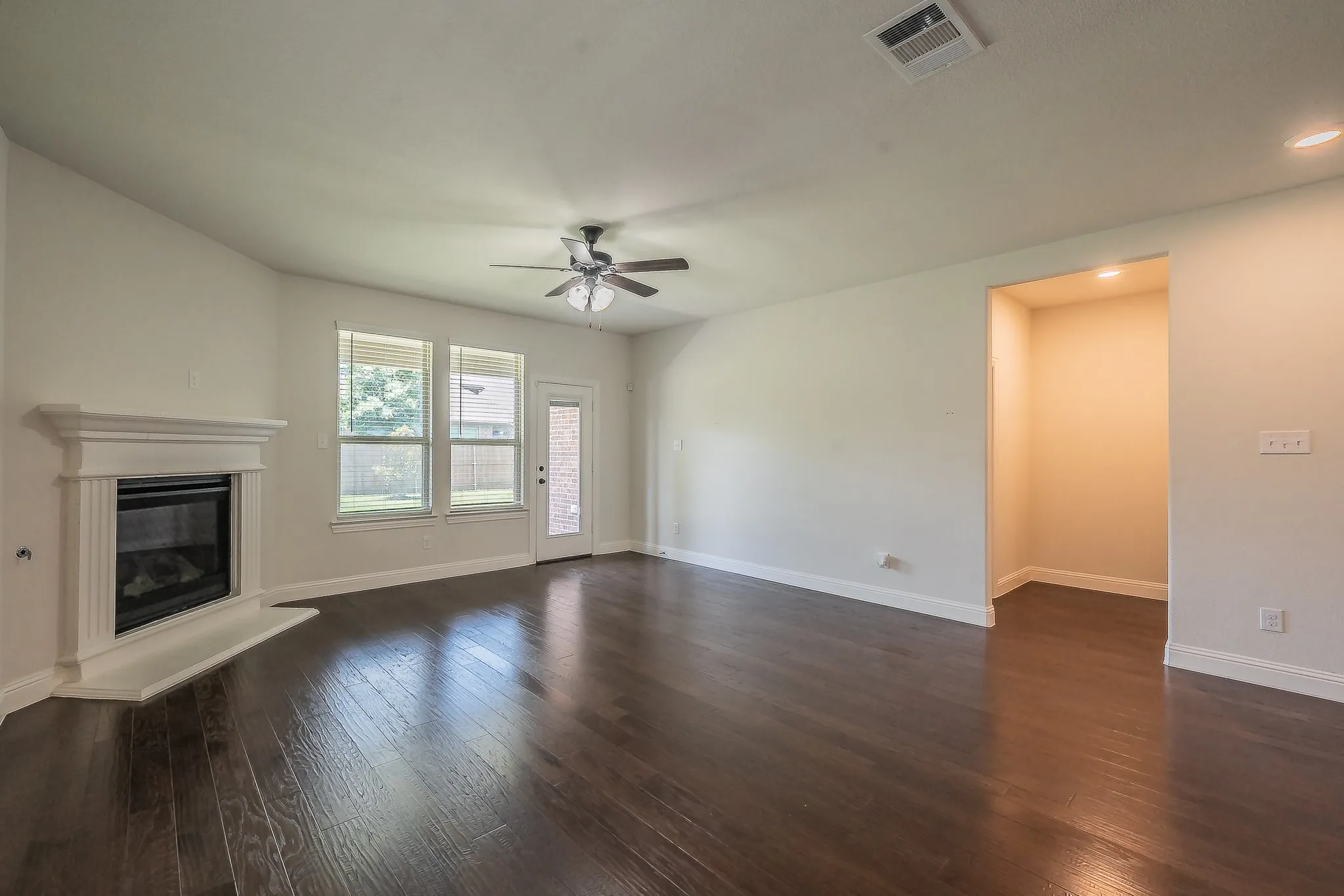 Spacious living area featuring dark wood-finish flooring, a white mantel fireplace, and a ceiling fan