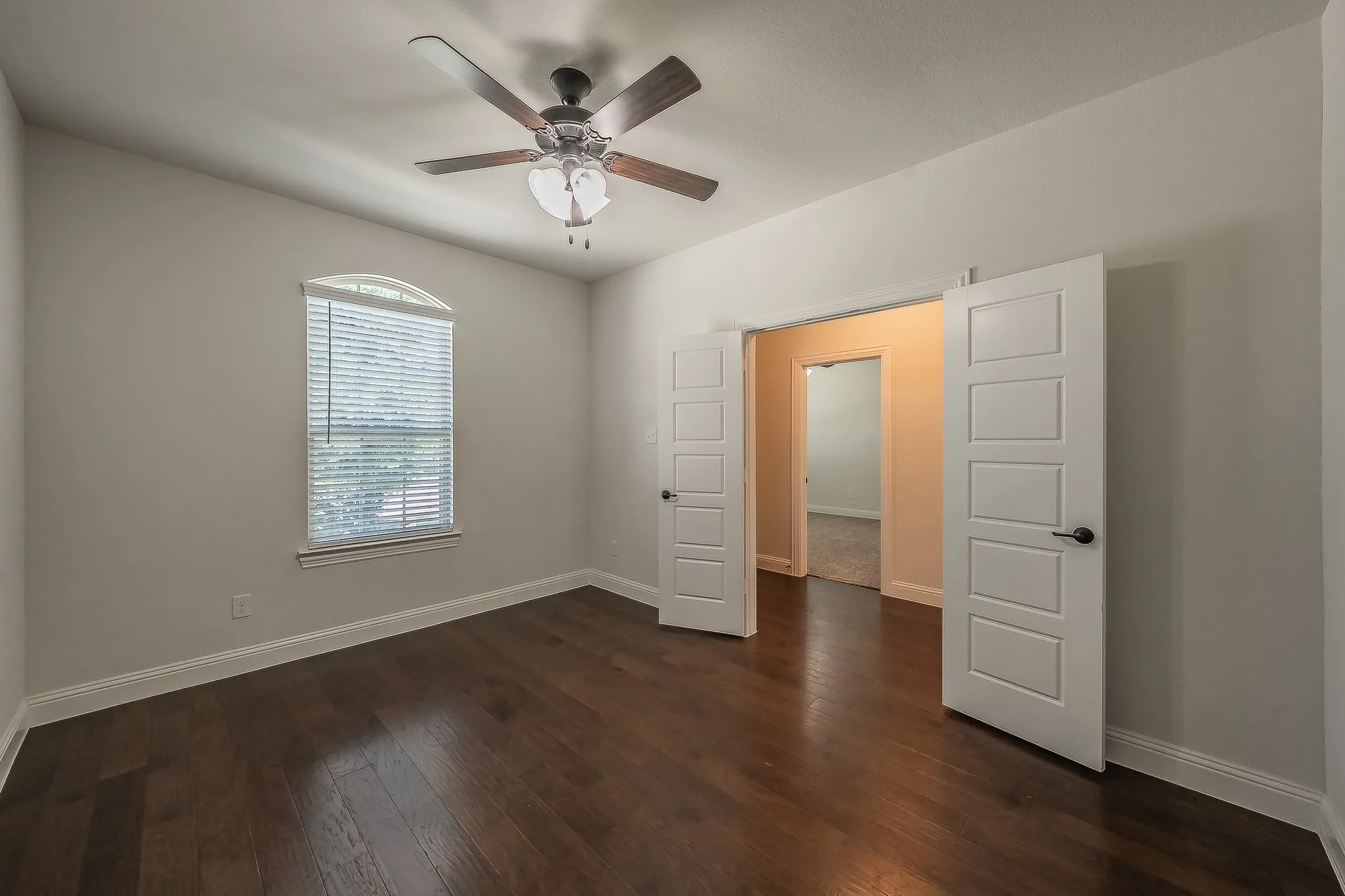 Spacious interior featuring wood-finish flooring, a contemporary ceiling fan with integrated lighting, and an arched window with blinds