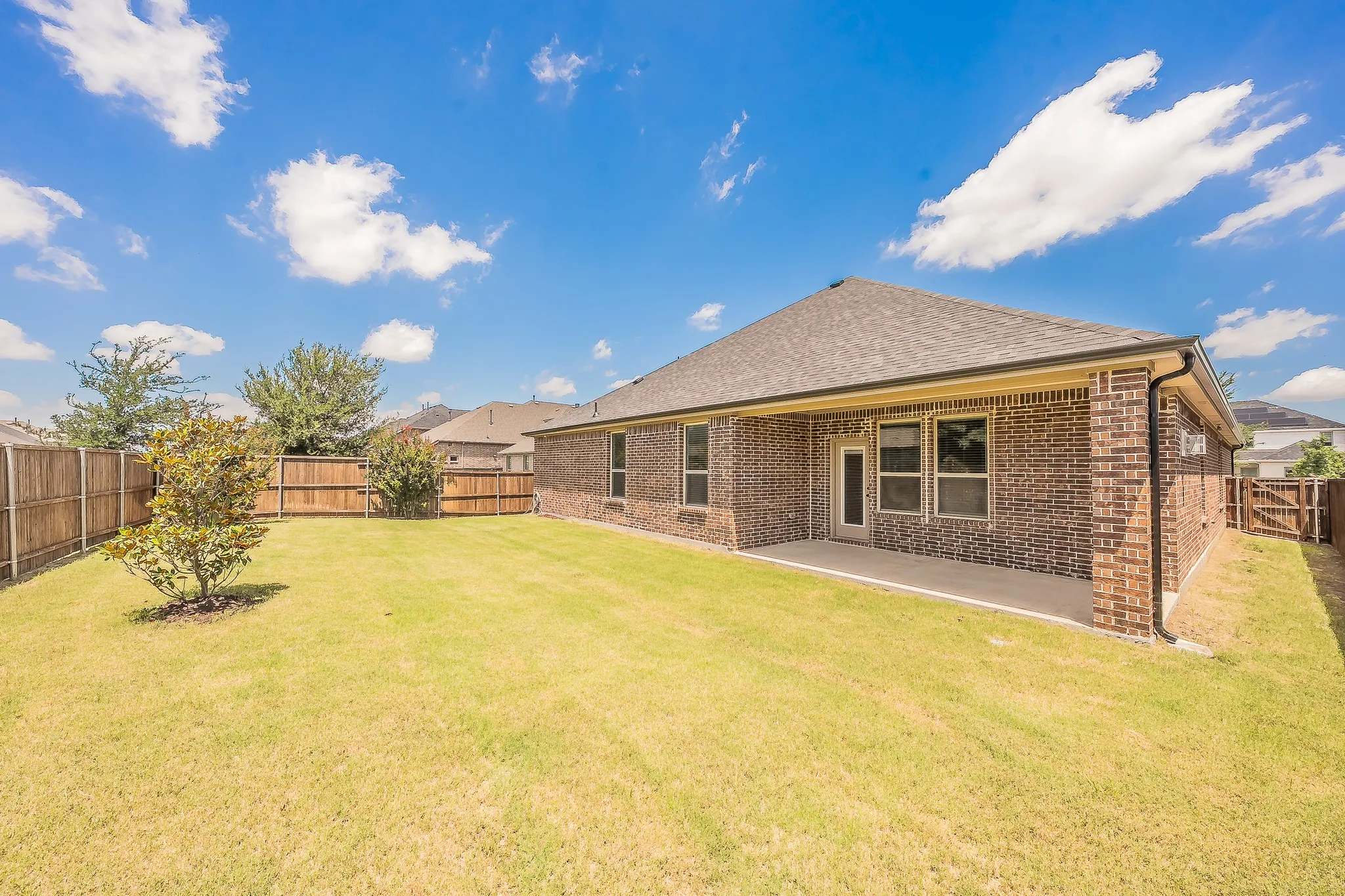Expansive backyard featuring a manicured lawn, full wood fencing, and a covered patio