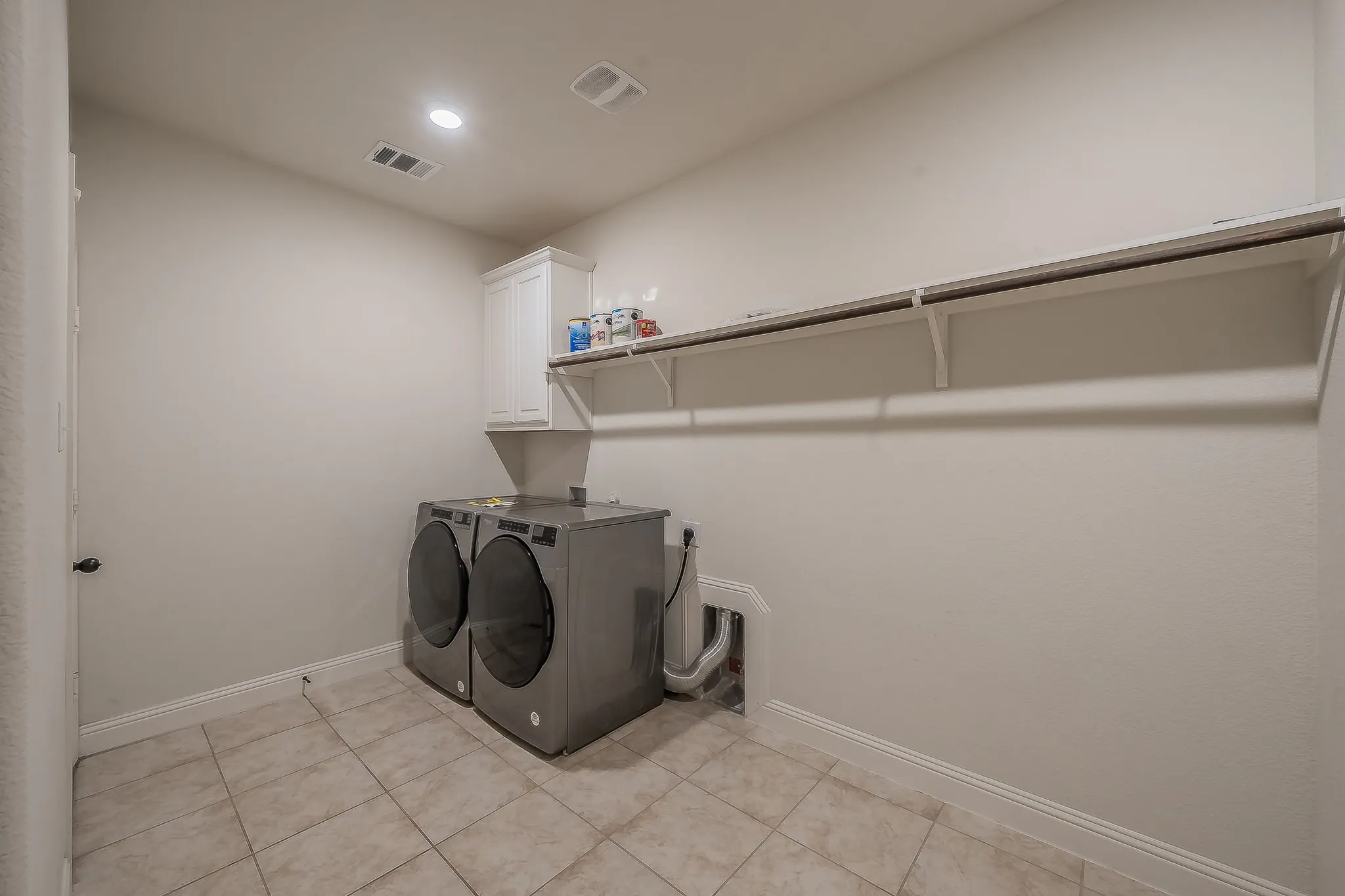 Dedicated laundry room featuring tile flooring, a built-in wall cabinet, and a wall-mounted shelving unit with a hanging rod