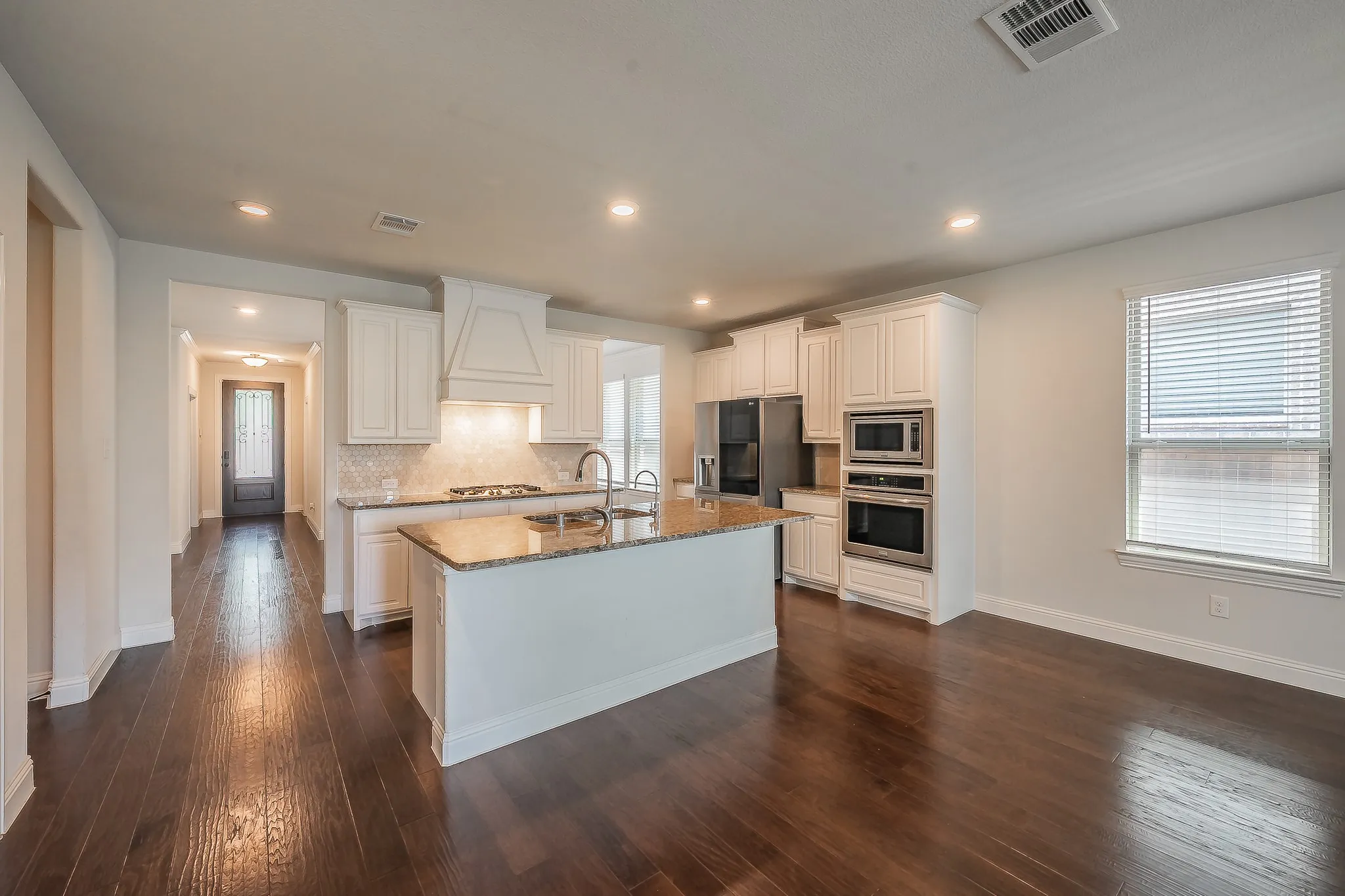 Open-concept kitchen featuring an island with a double basin sink, white cabinetry, integrated stainless steel appliances, and wood-finish flooring
