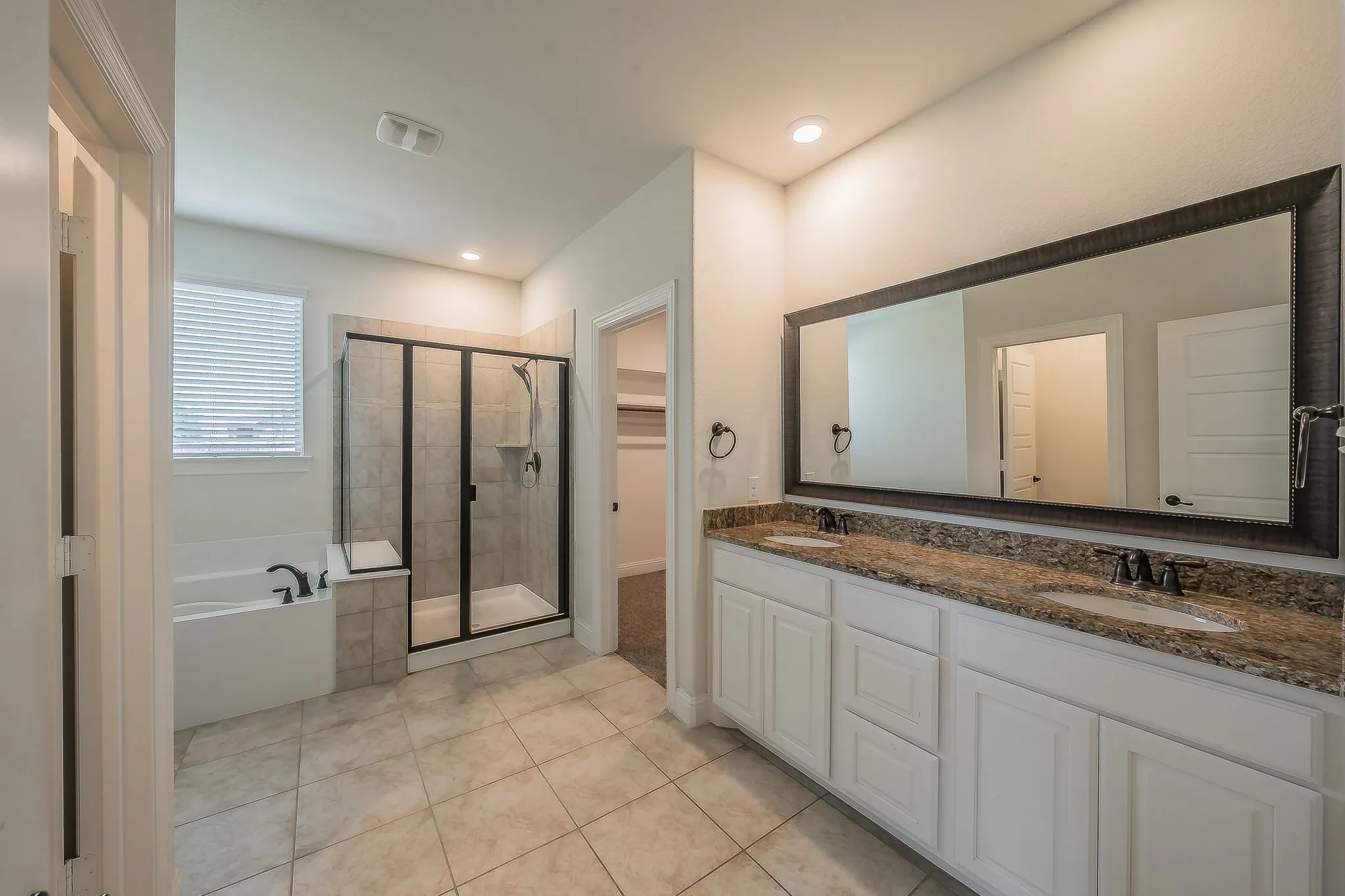 Spacious bathroom featuring a dual vanity with a stone countertop, an oversized framed mirror, a separate soaking tub, and a glass-enclosed shower with tiled walls