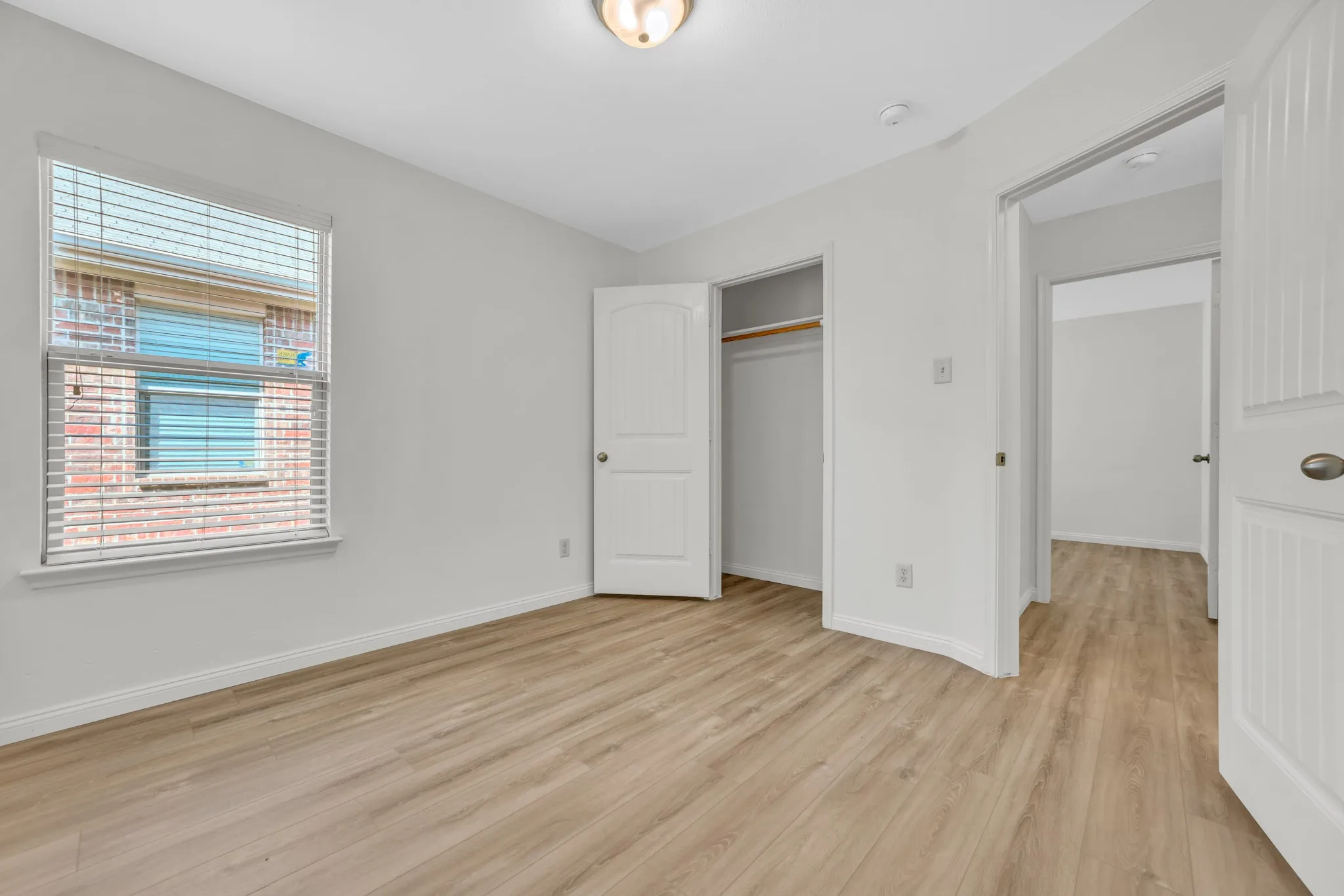 Light wood-finish flooring extends throughout this room, featuring a window with blinds and a built-in closet