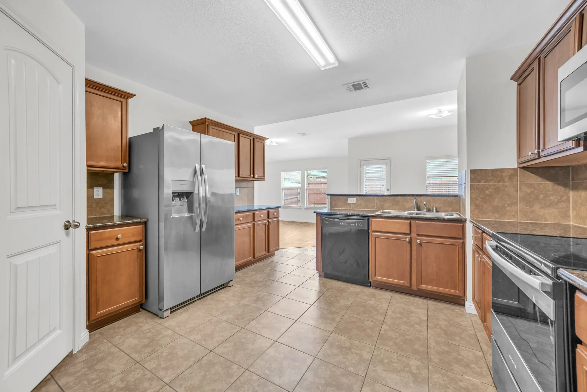 Kitchen featuring tile flooring, wooden cabinetry, stone-finish countertops, and a tile backsplash