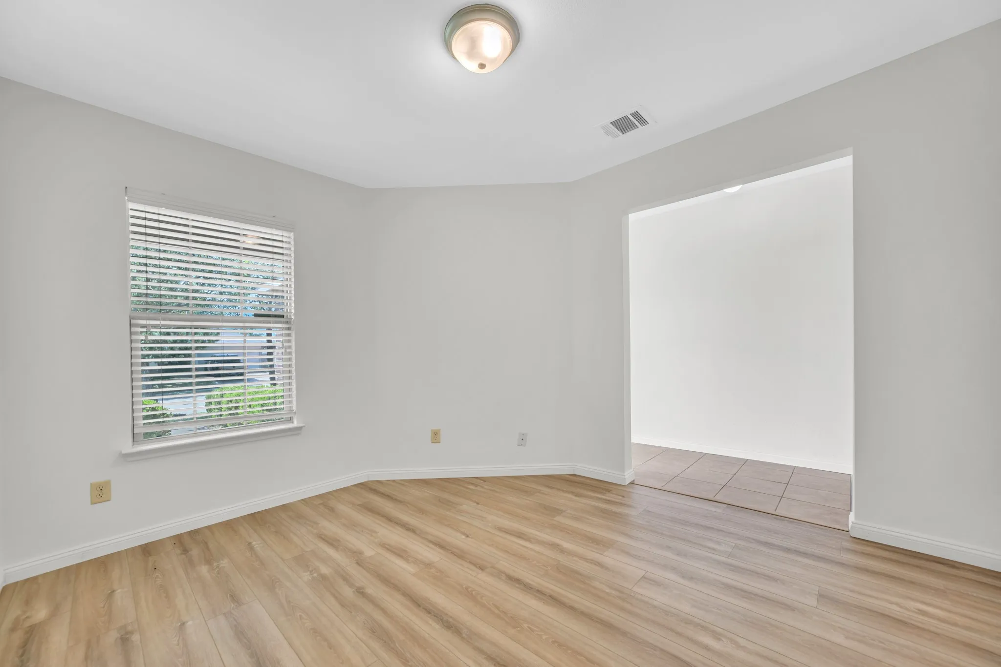 Room featuring wood-finish flooring, white baseboards, and a single window with blinds