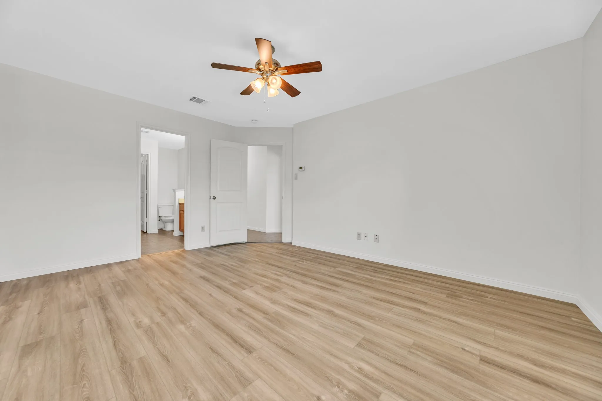 Spacious room featuring light wood-finish flooring, a ceiling fan with integrated lighting, and crisp white walls