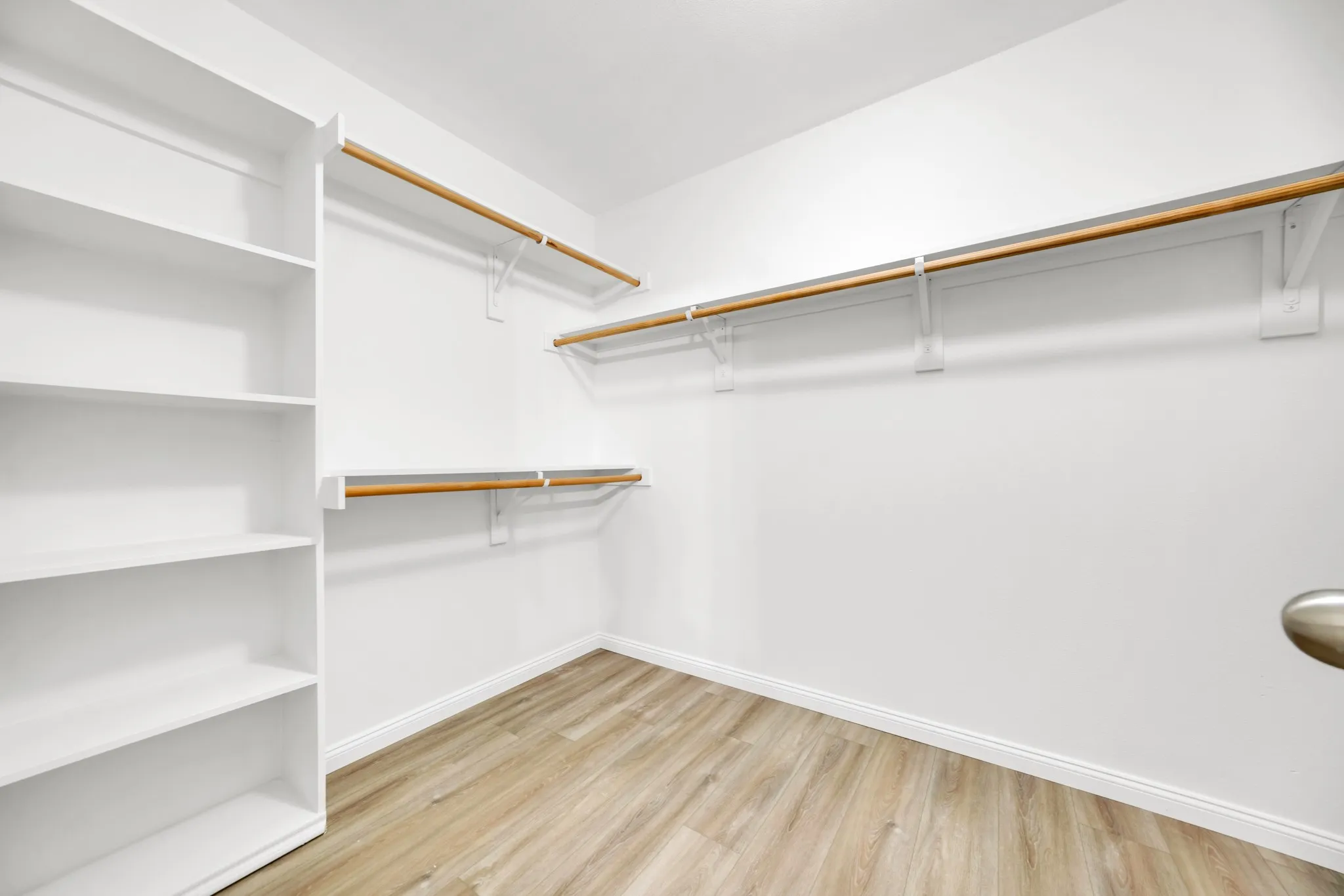 Open closet featuring extensive built-in shelving, multiple hanging rods, and wood-finish flooring