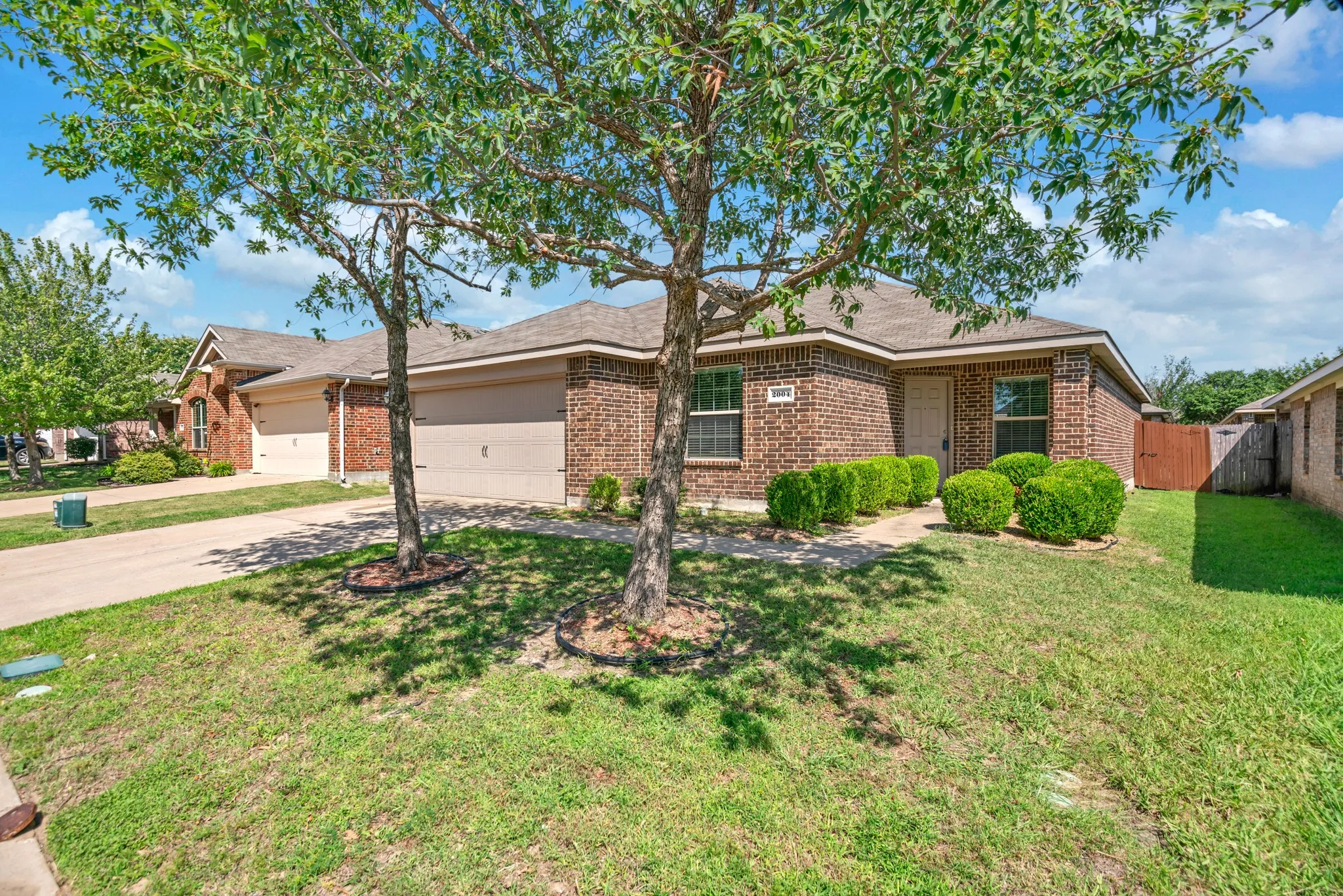 Brick exterior residence with a two-car garage, mature trees, and a well-maintained lawn