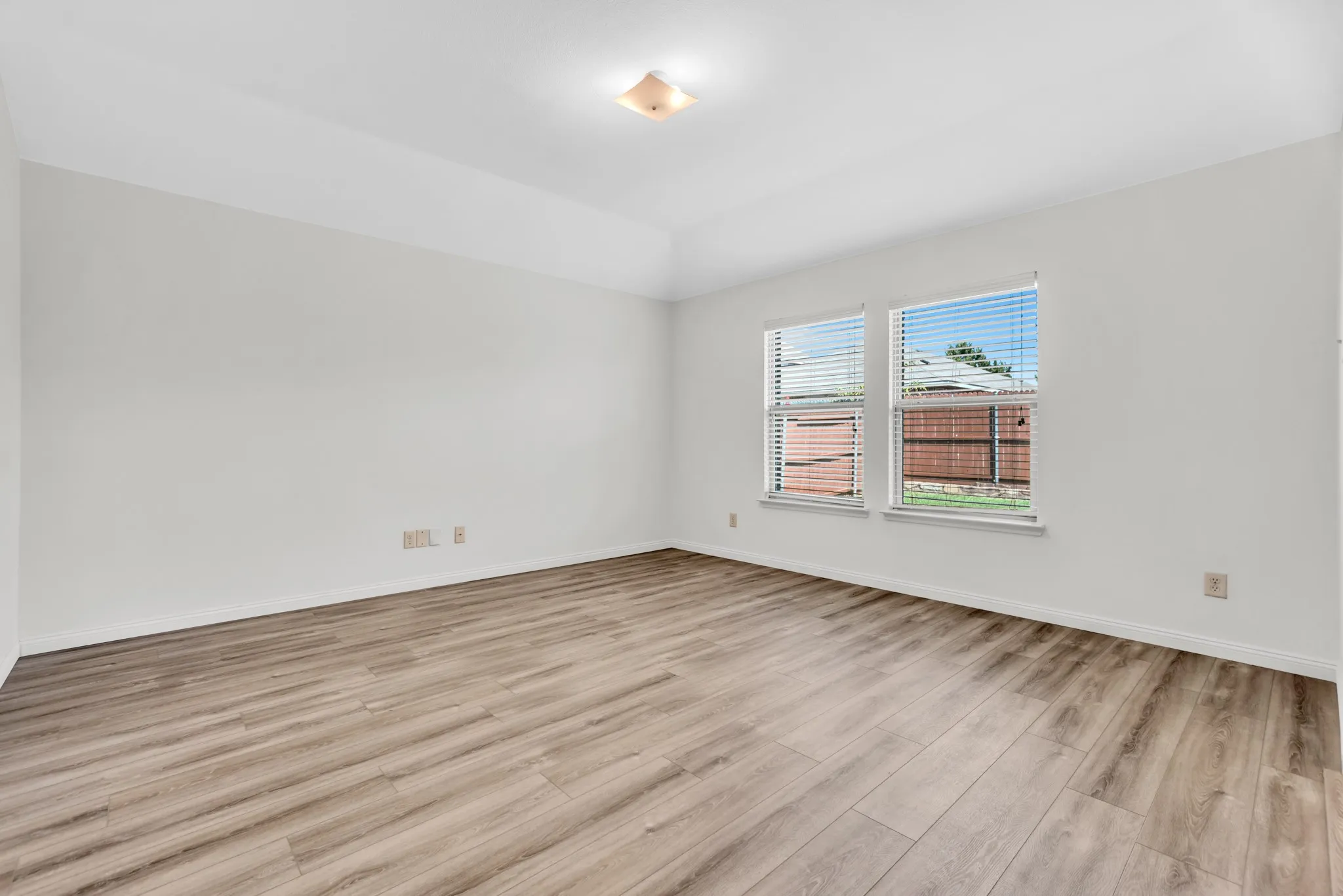 Spacious room featuring wood-finish flooring, light-colored walls, and a tray ceiling