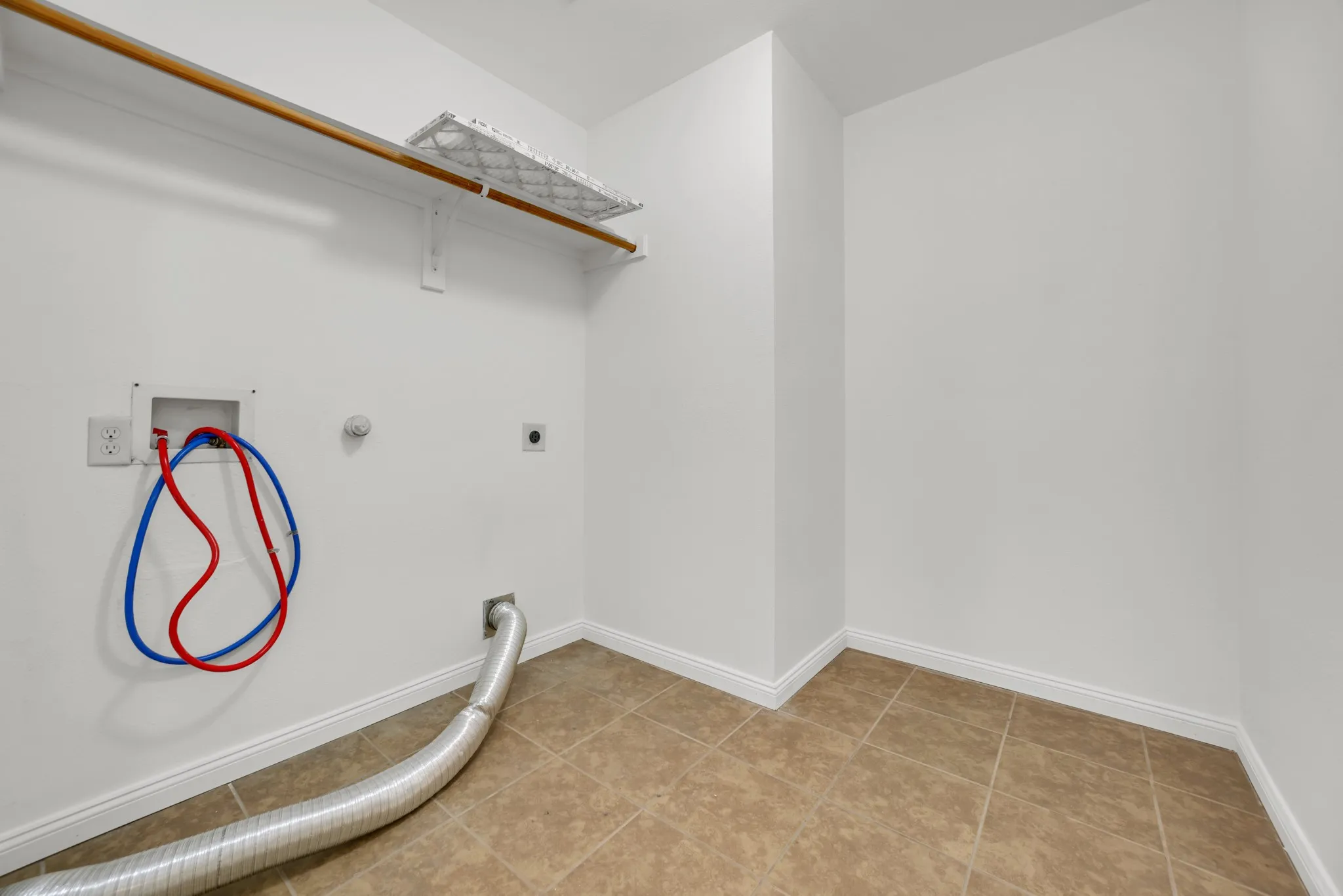 Laundry area featuring white walls, tile flooring, a wood-finish clothes rod, and a built-in shelf
