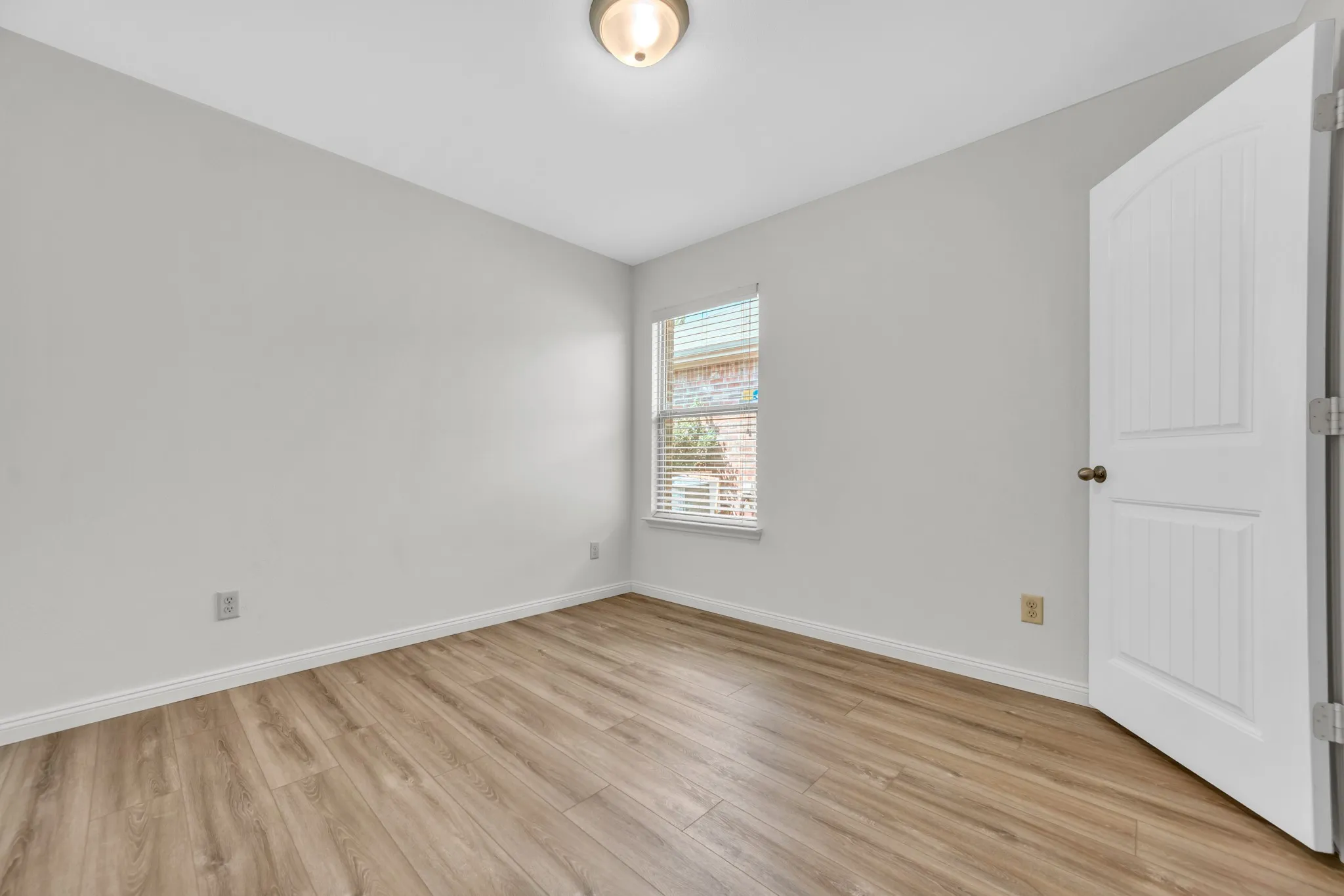 Neutral-toned room featuring wood-finish flooring and a single window with blinds