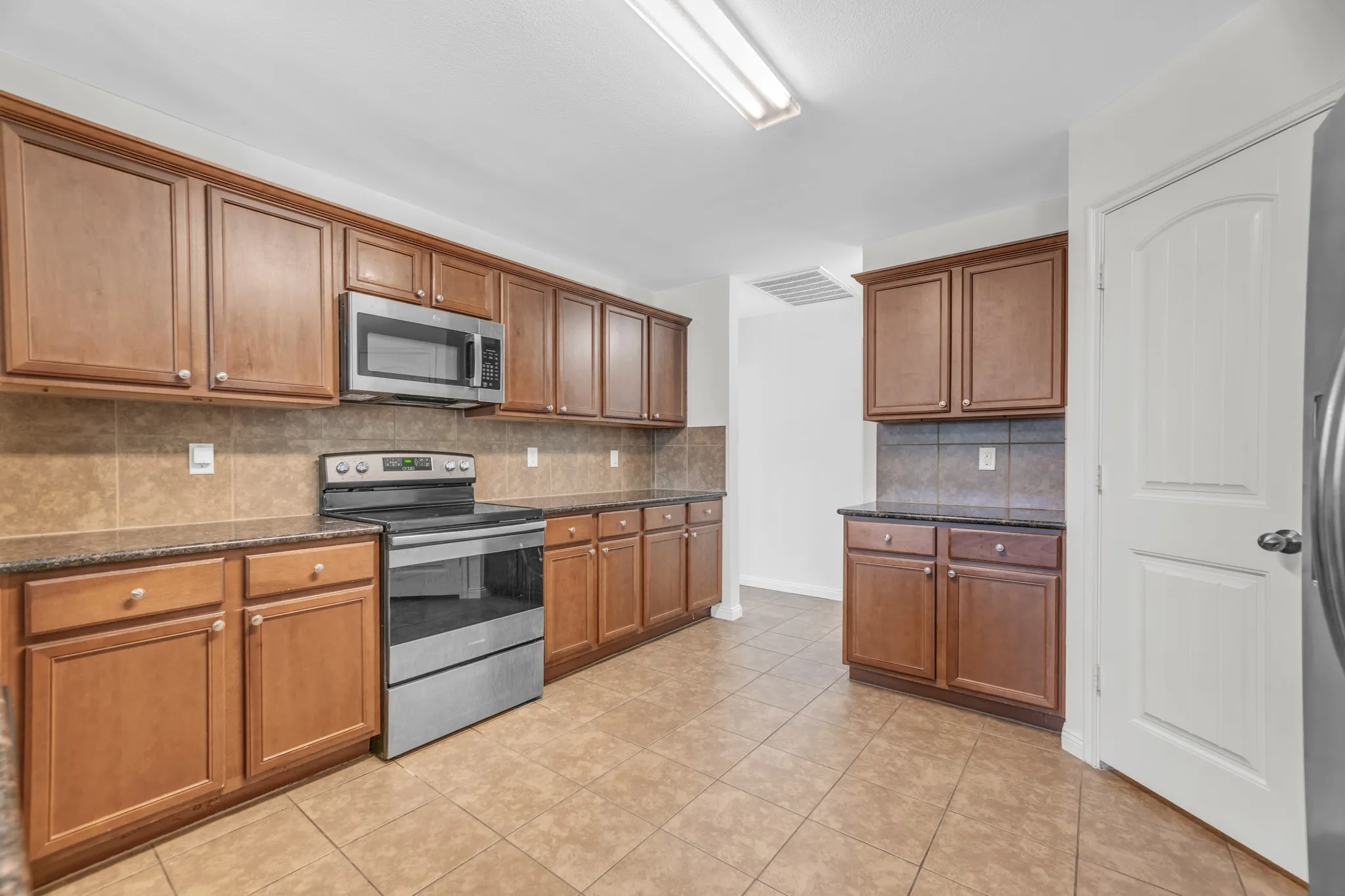 Kitchen featuring extensive wood cabinetry, tile flooring, stone-finish countertops, stainless steel appliances, and a tiled backsplash