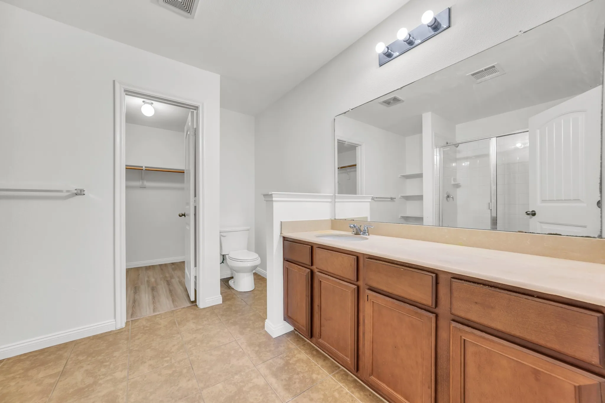 Bathroom featuring a double vanity with wood cabinetry, light-toned countertop, and an expansive mirror