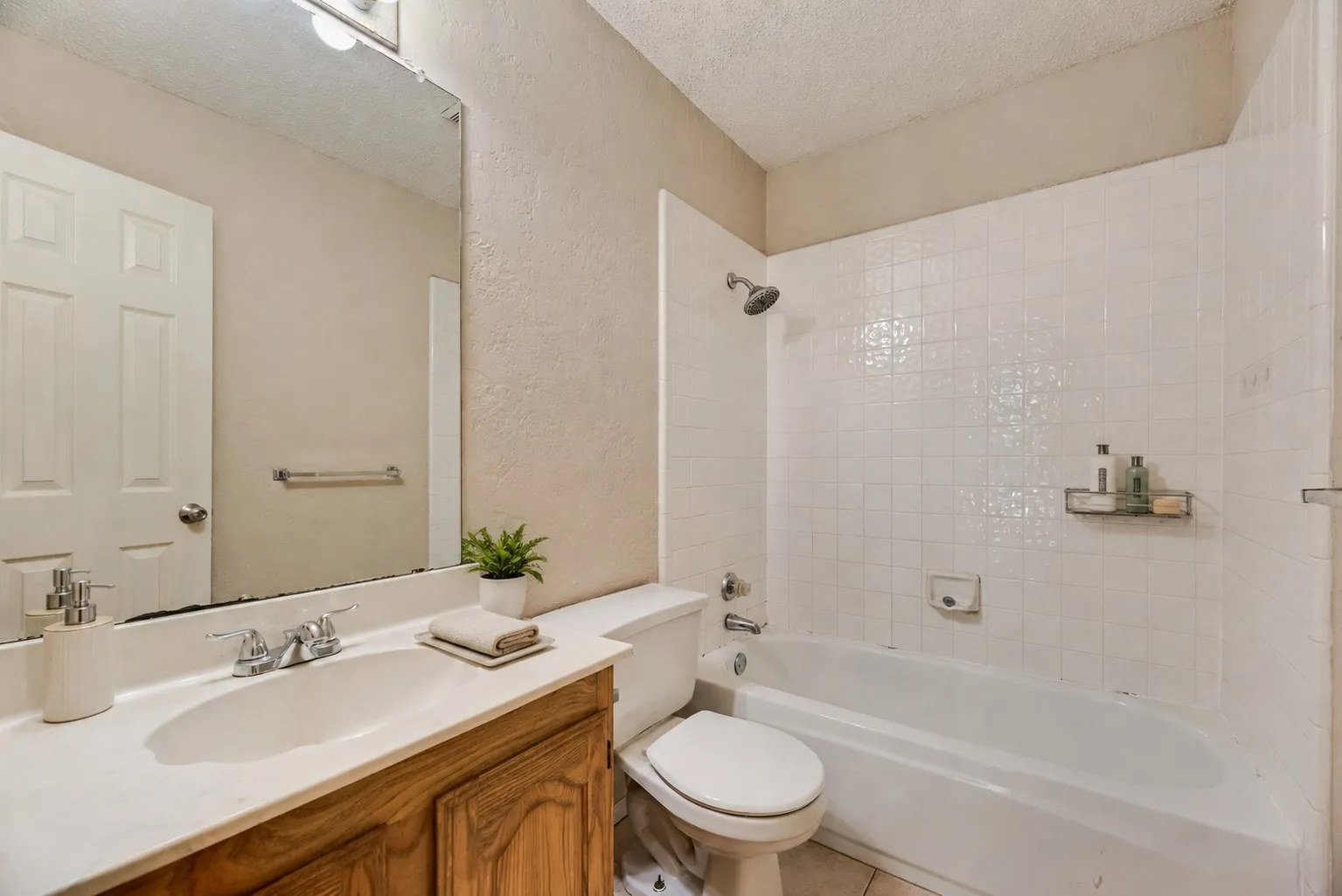 Bathroom featuring a white bathtub with subway tile surround, a chrome shower head, a wood-finish vanity with an integrated sink, a large wall-mounted mirror, and a white toilet