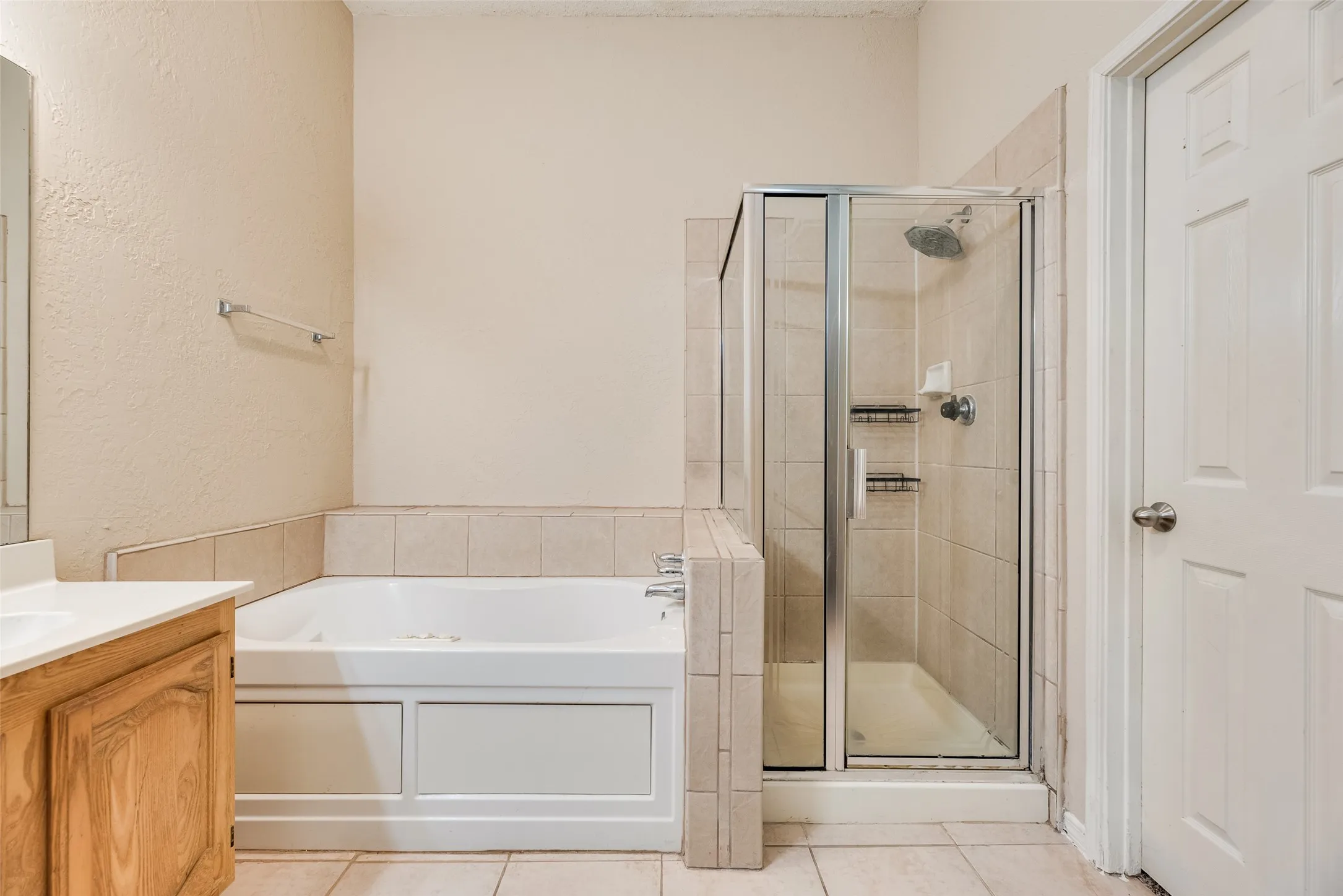 Bathroom featuring a tiled shower with glass enclosure, a built-in bathtub with a tiled surround, a light wood-finish vanity with a white countertop, and tile flooring