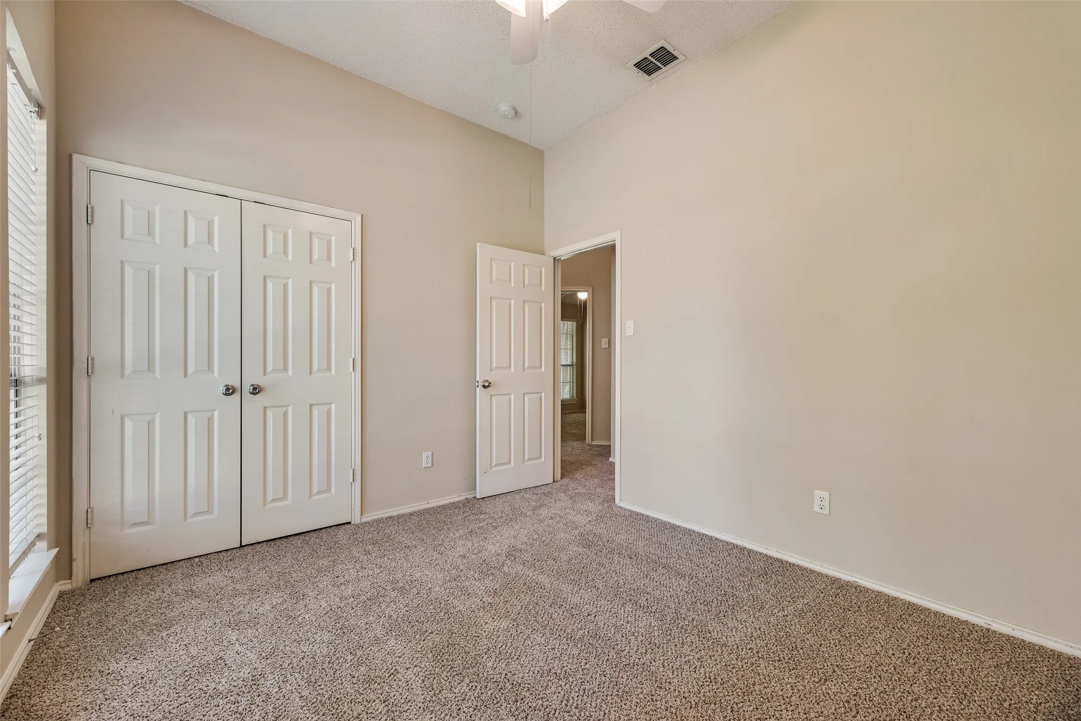 Interior room featuring vaulted ceilings, neutral tone carpeting, and a window with horizontal blinds