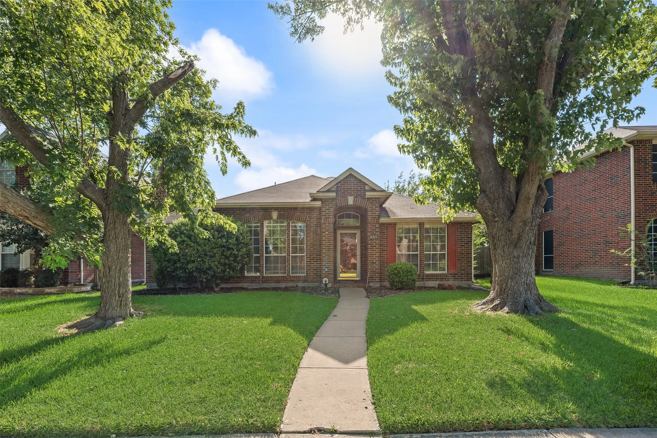 Brick exterior with a central arched entry, mature front yard trees, and a concrete pathway