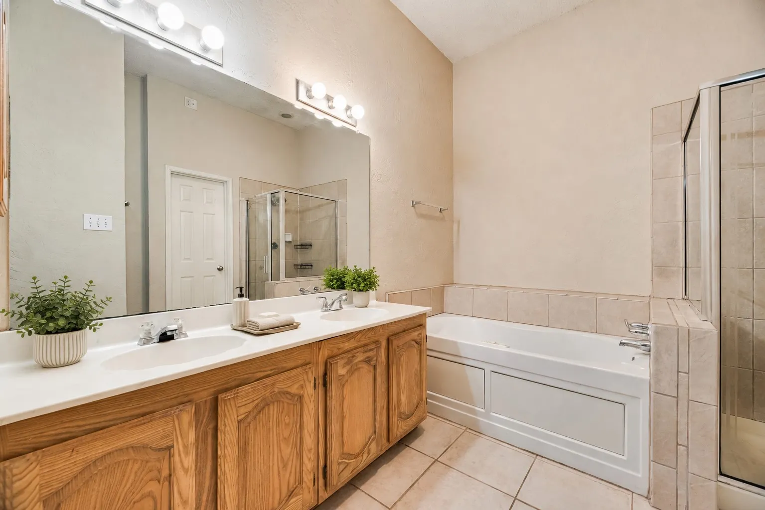 Bathroom featuring a double vanity with wood cabinetry, a large integrated mirror, and dual light fixtures