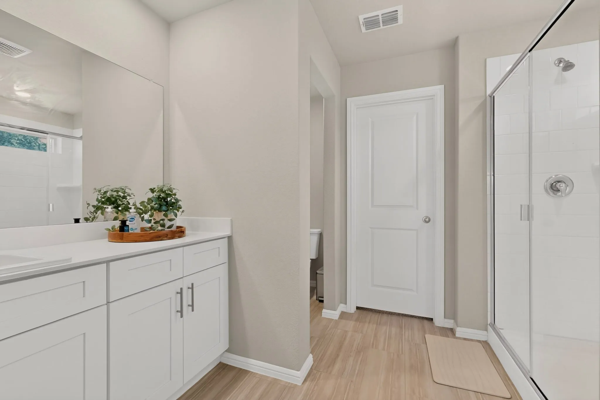 Bathroom featuring a double vanity with white cabinetry, a large wall-mounted mirror, and a glass-enclosed shower with subway tile