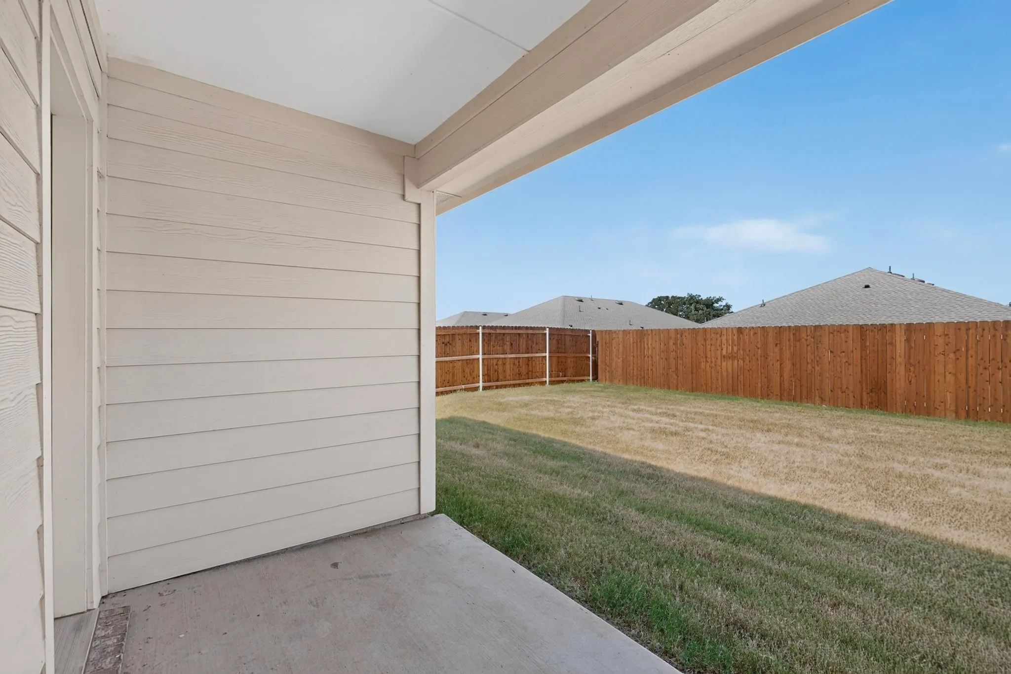 Covered concrete patio extending to a fenced yard
