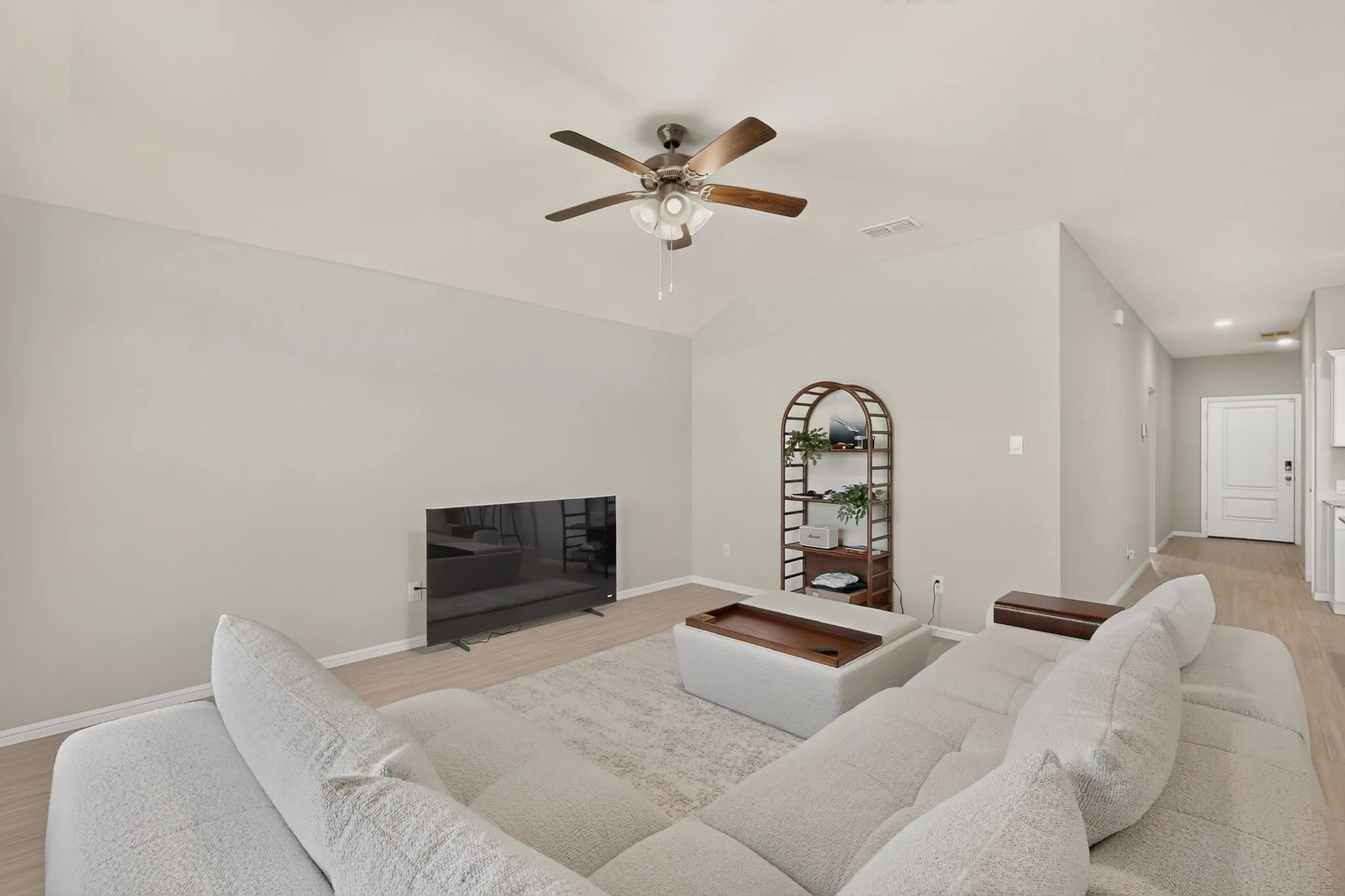 Spacious living area featuring light-colored walls, wood-finish flooring, and a vaulted ceiling