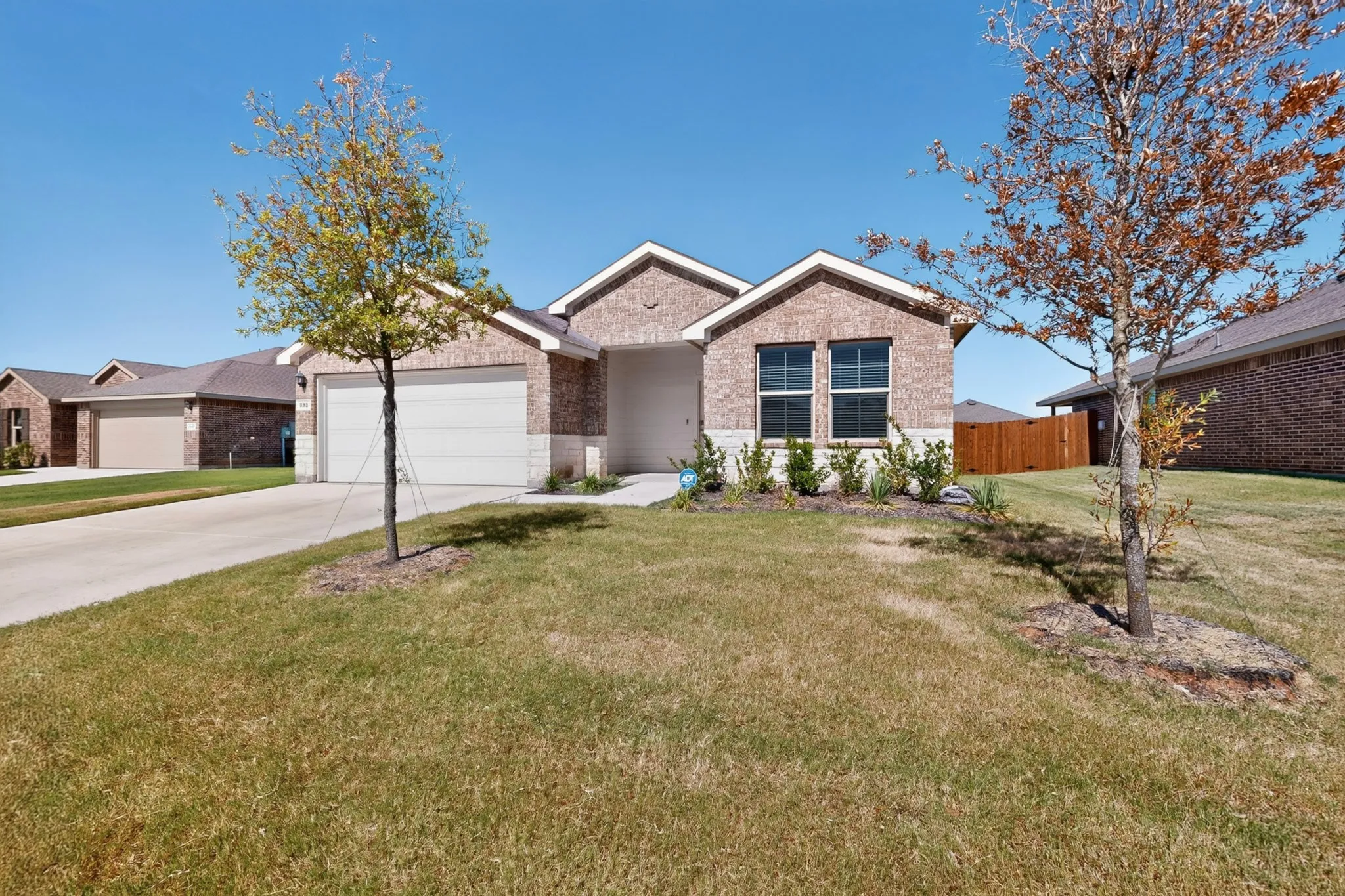 Brick facade residence featuring a two-car garage, manicured front landscaping, and a concrete driveway
