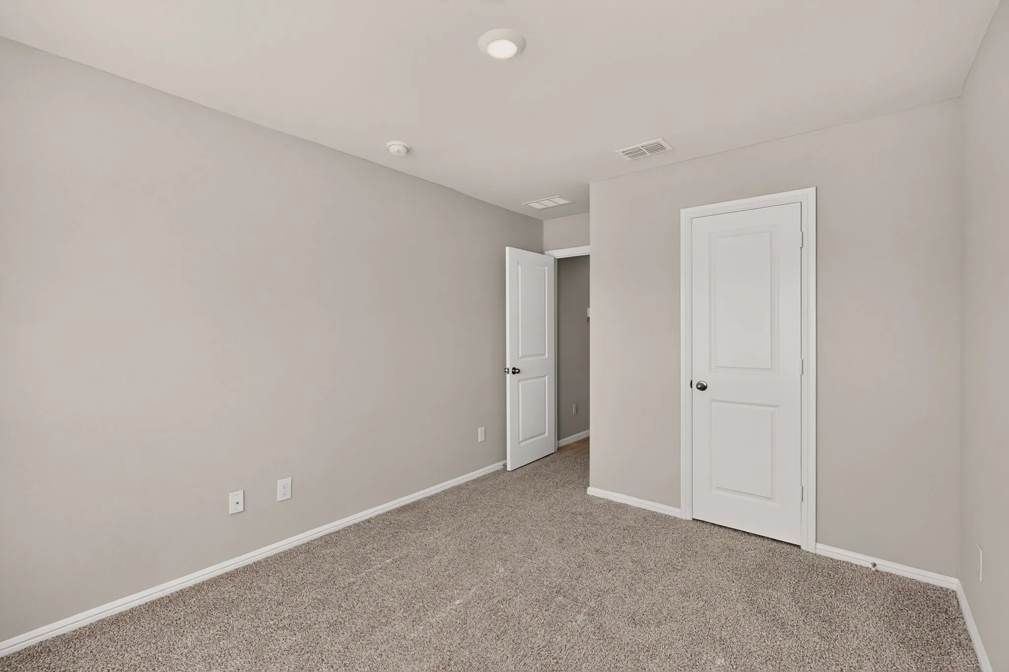 Carpeted room featuring light gray walls, white baseboards, and a white paneled door with a black doorknob