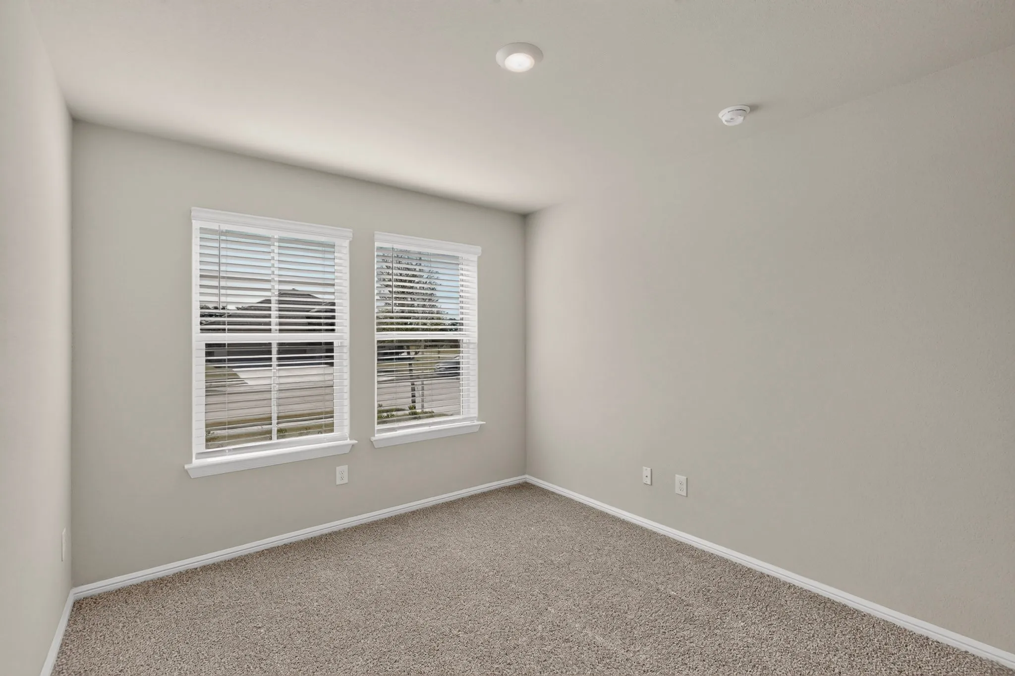 Neutral-toned room featuring a soft carpeted floor and two windows with white blinds
