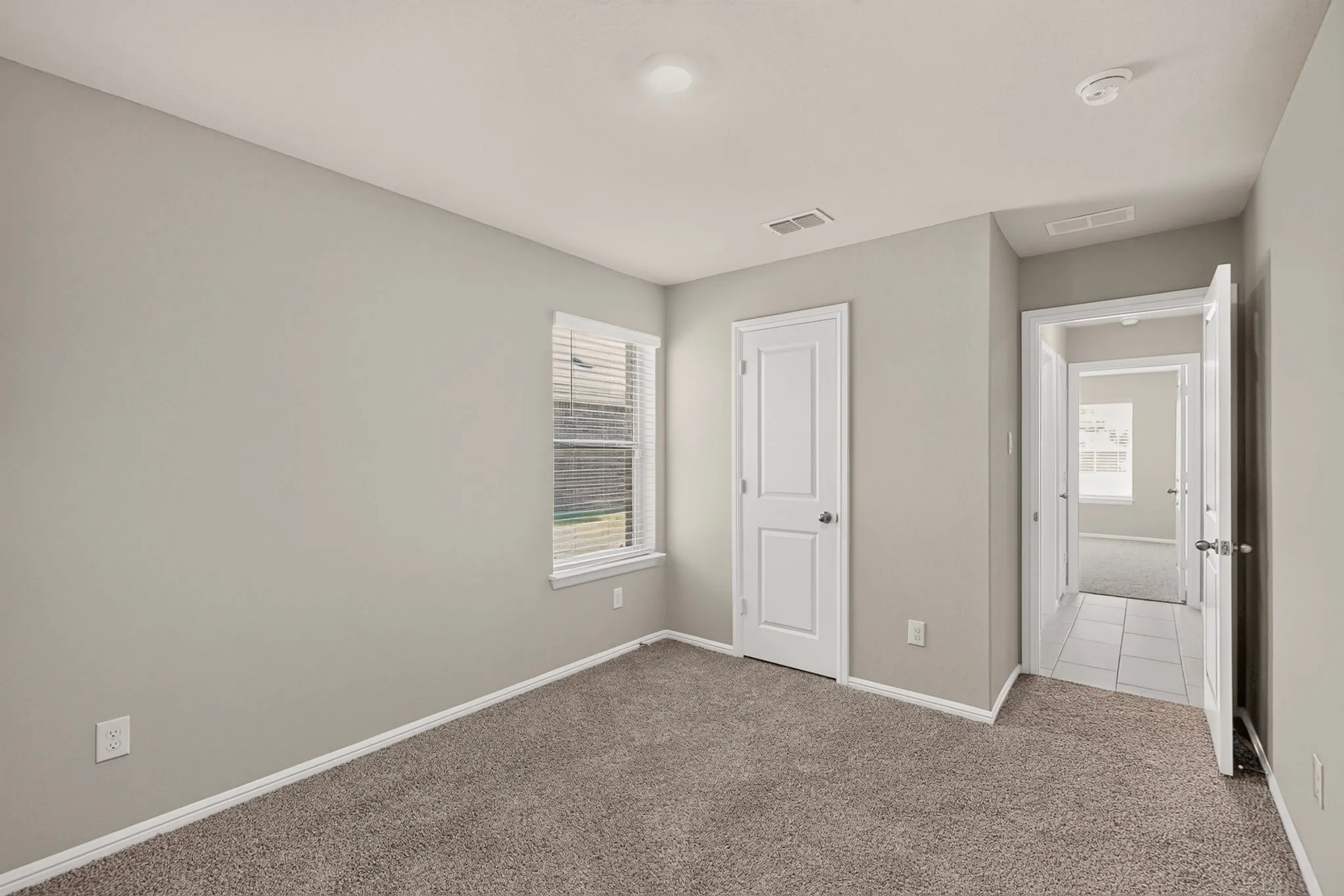 Carpeted room featuring a single window with blinds, a white paneled door, and neutral gray walls