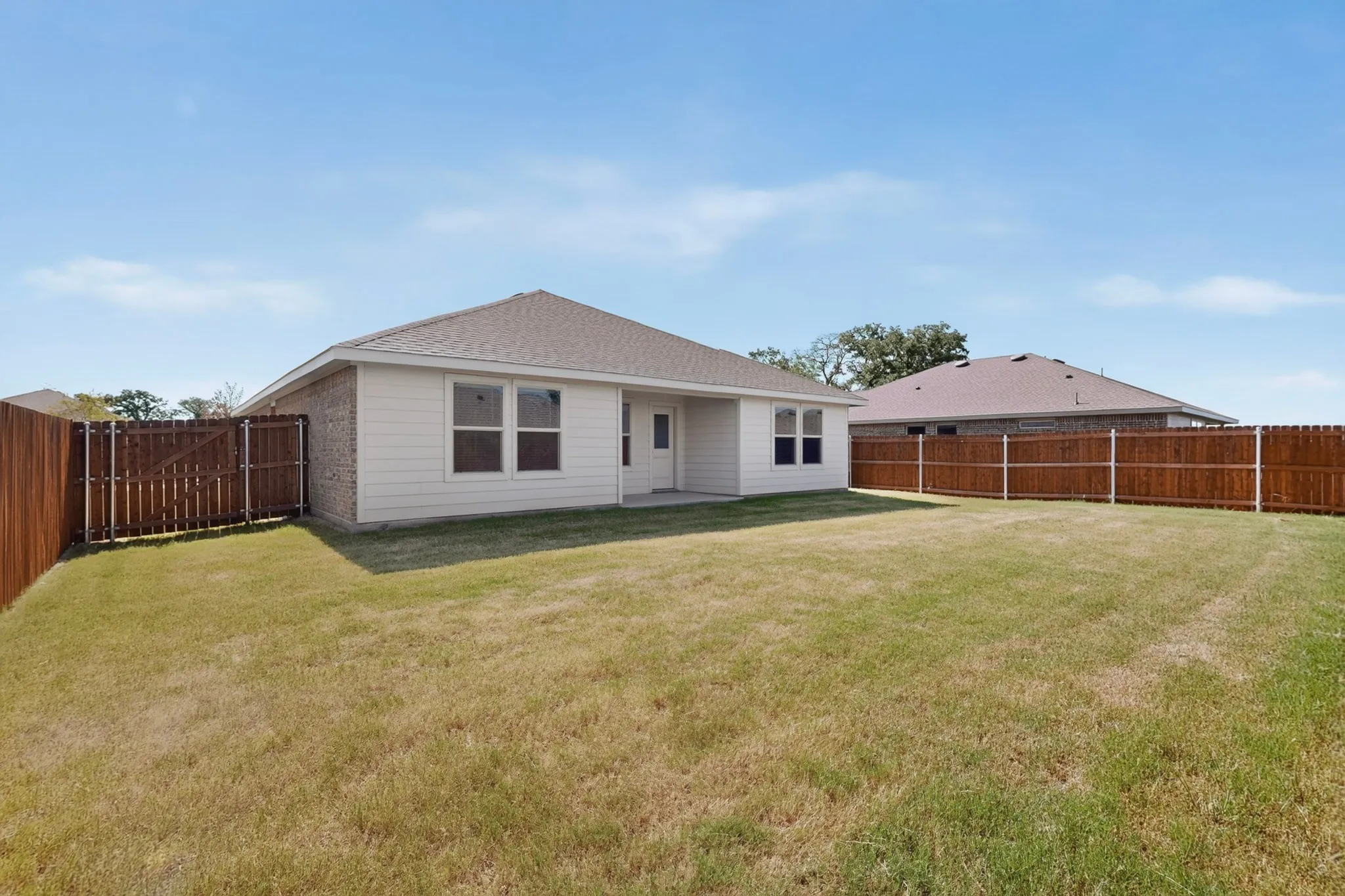 Expansive backyard featuring a natural grass lawn, full perimeter wood fencing, and a rear patio