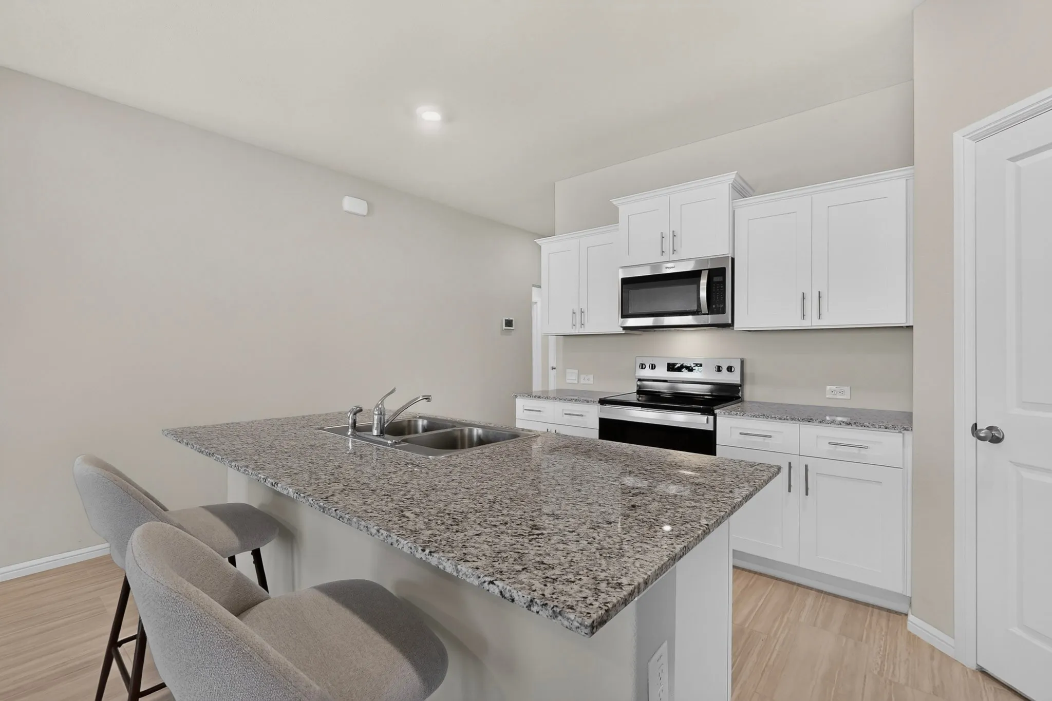 Kitchen featuring a center island with a double basin stainless steel sink, granite countertops, white shaker cabinetry, stainless steel appliances, and wood-finish flooring