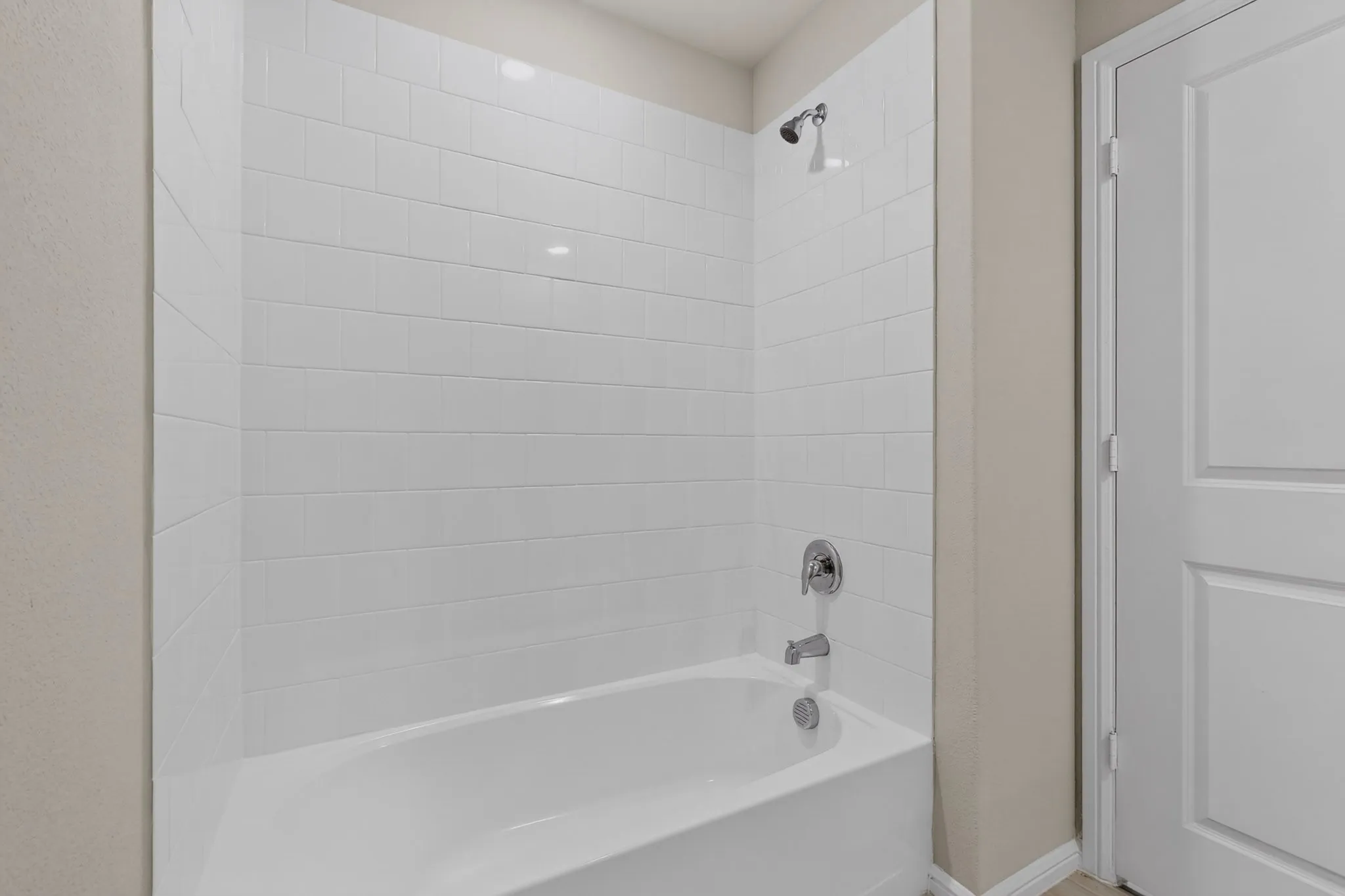Bathtub with white subway tile surround, chrome fixtures, and a shower head