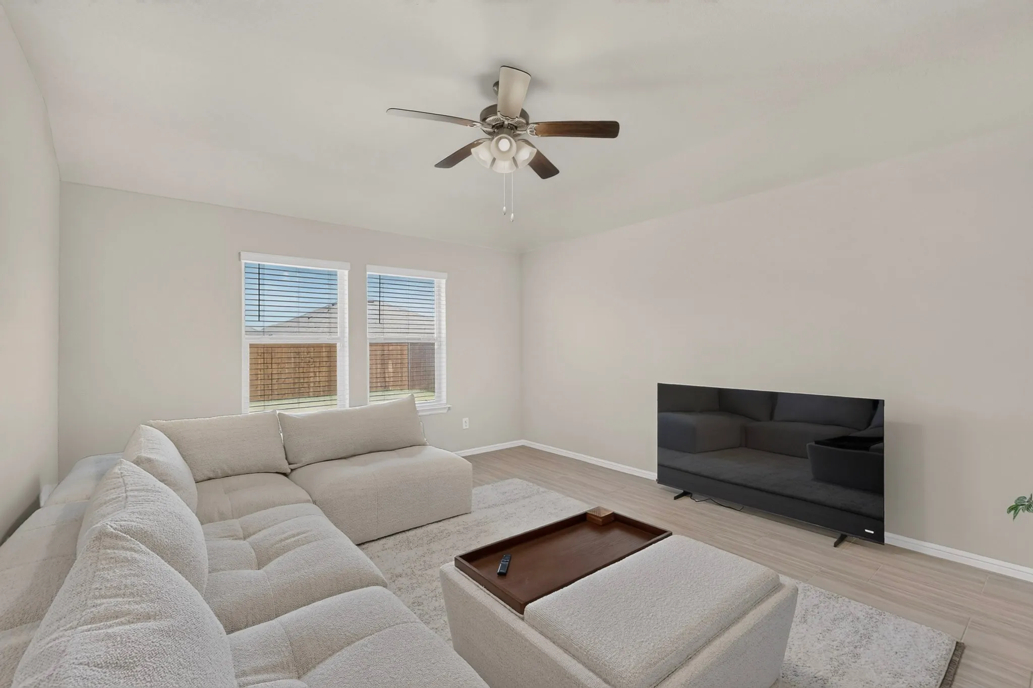 Living area featuring neutral wall tones, wood-finish flooring, and two windows with blinds