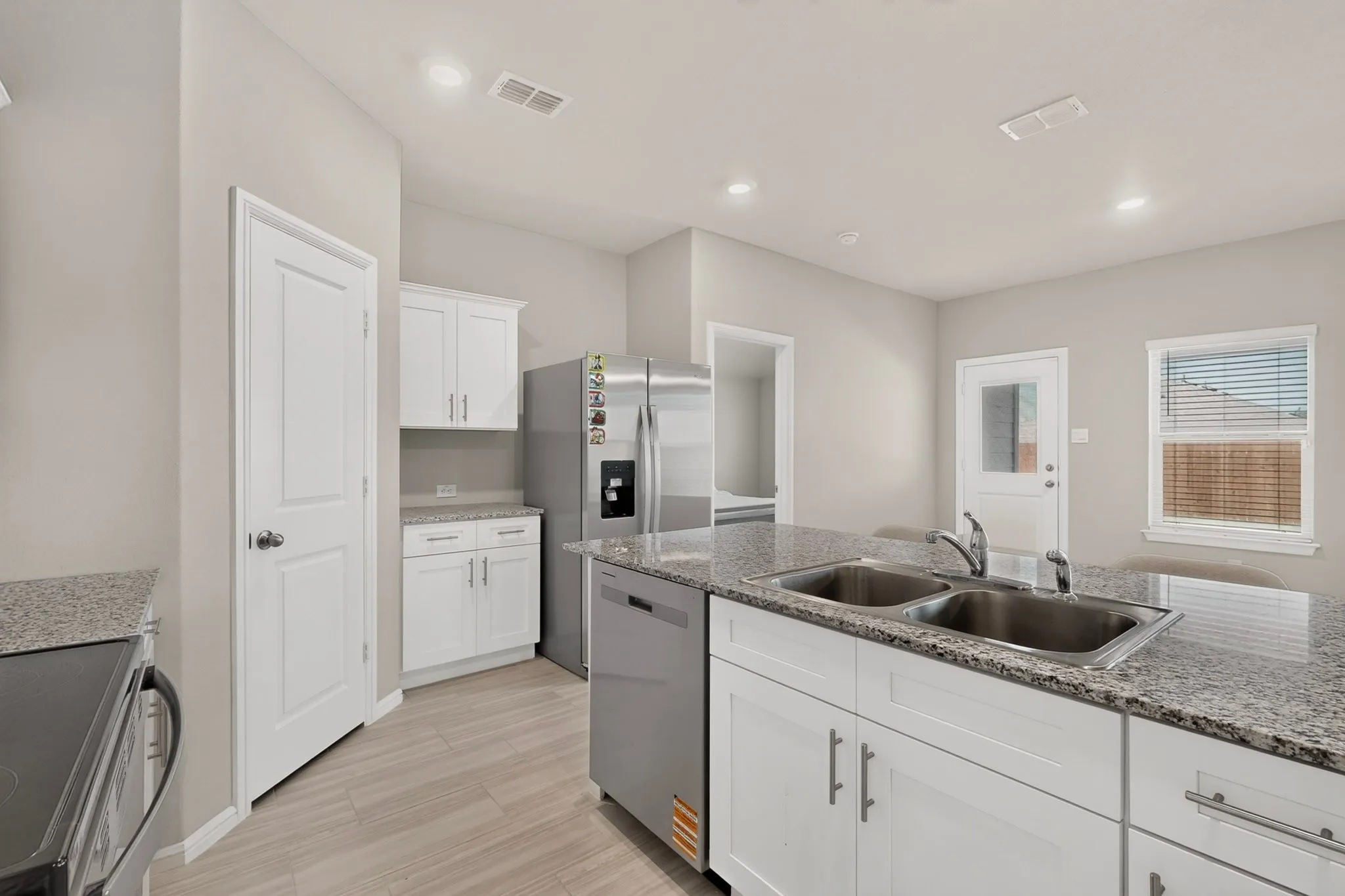 Modern kitchen featuring light wood-finish flooring, white cabinetry, granite countertops, and stainless steel appliances
