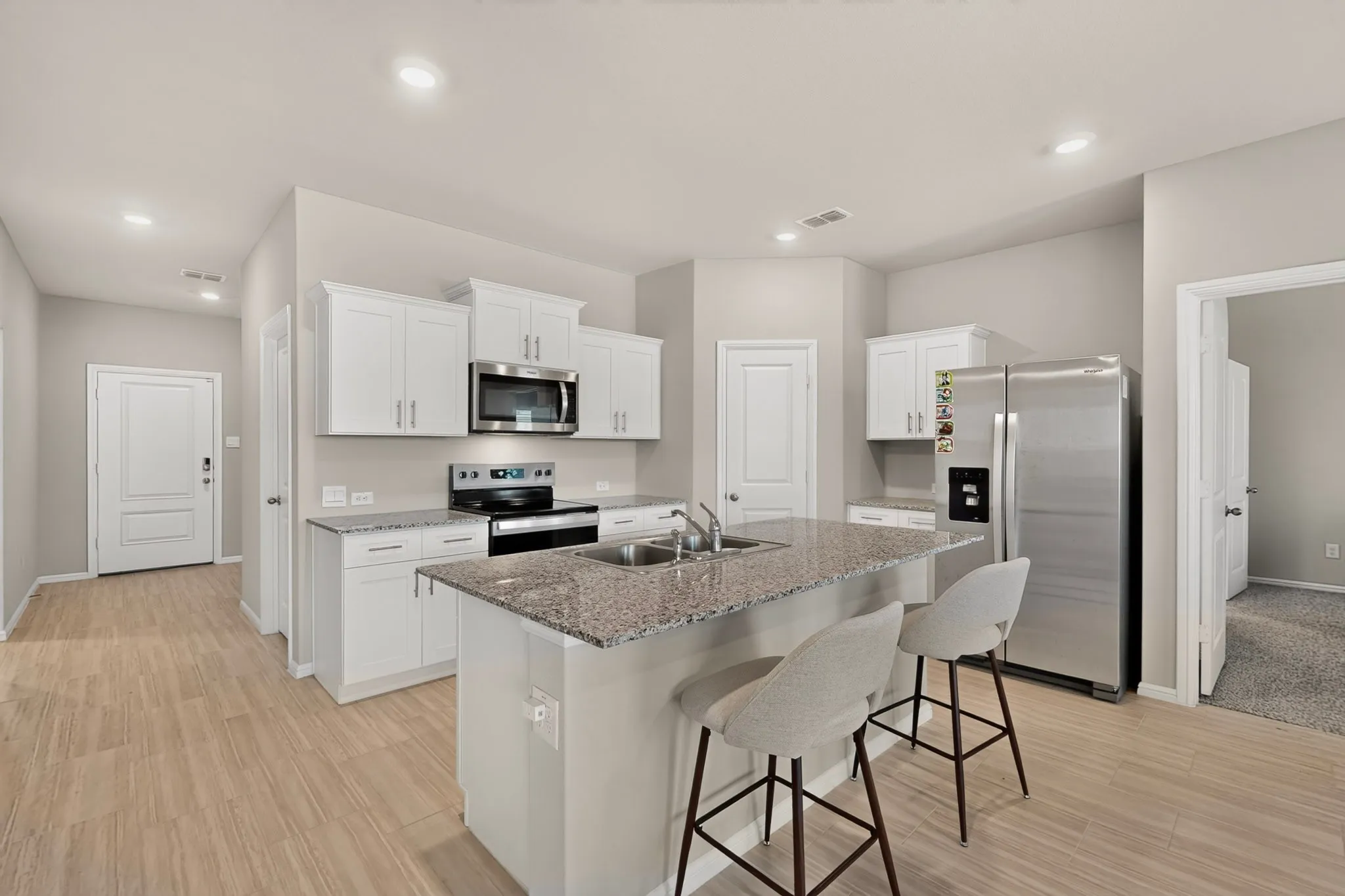 Kitchen featuring an island with a double basin sink, granite countertops, white cabinetry, wood-finish flooring, and stainless steel appliances
