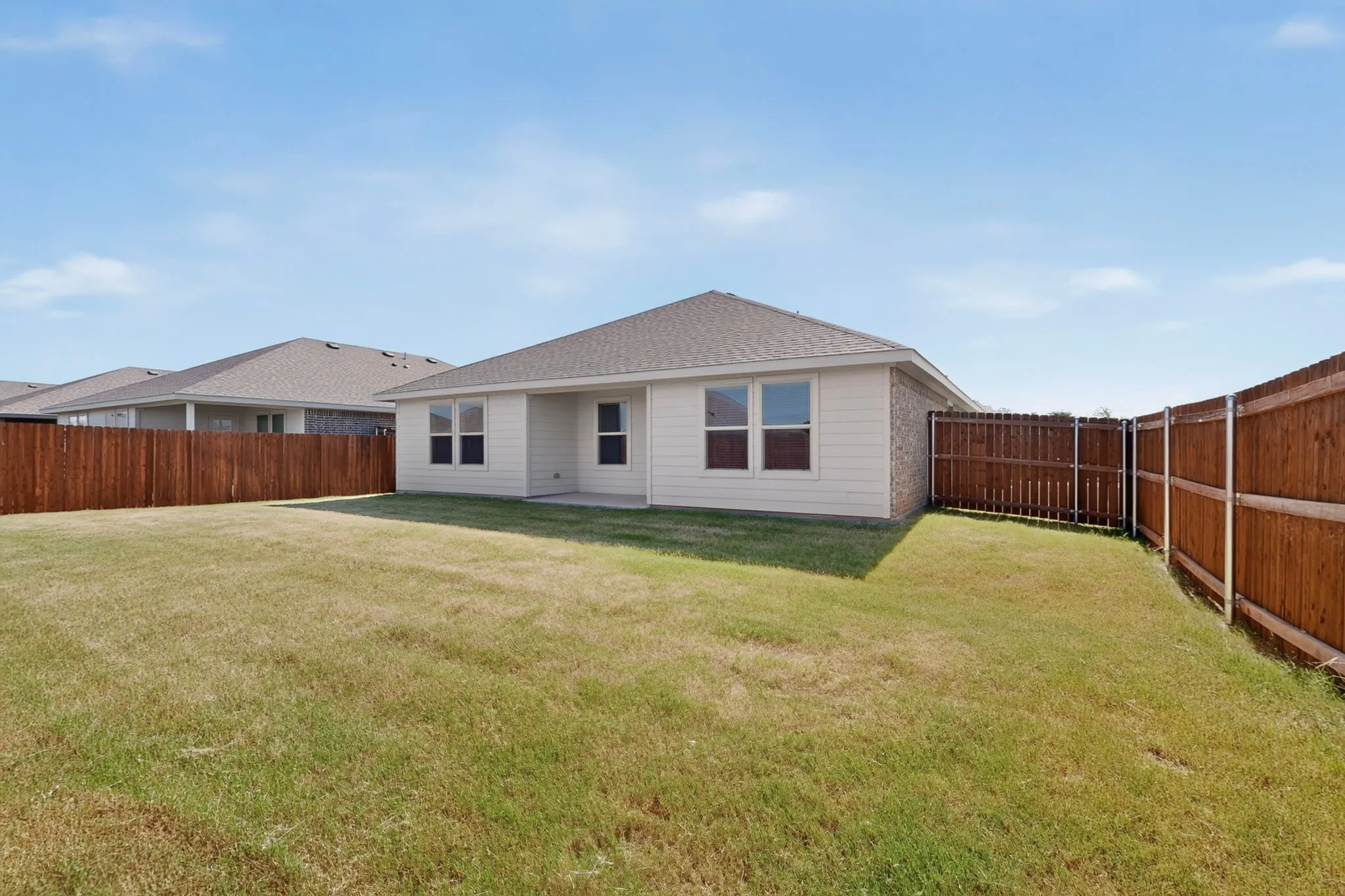 Expansive rear yard featuring a privacy fence, a concrete patio, and multiple window openings