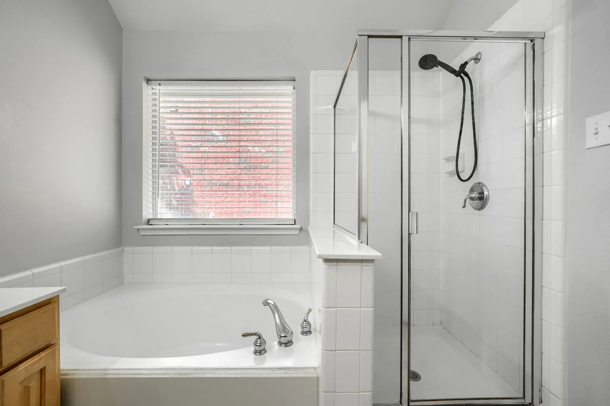 Soaking tub with white tile surround, adjacent to a glass-enclosed shower with a handheld showerhead