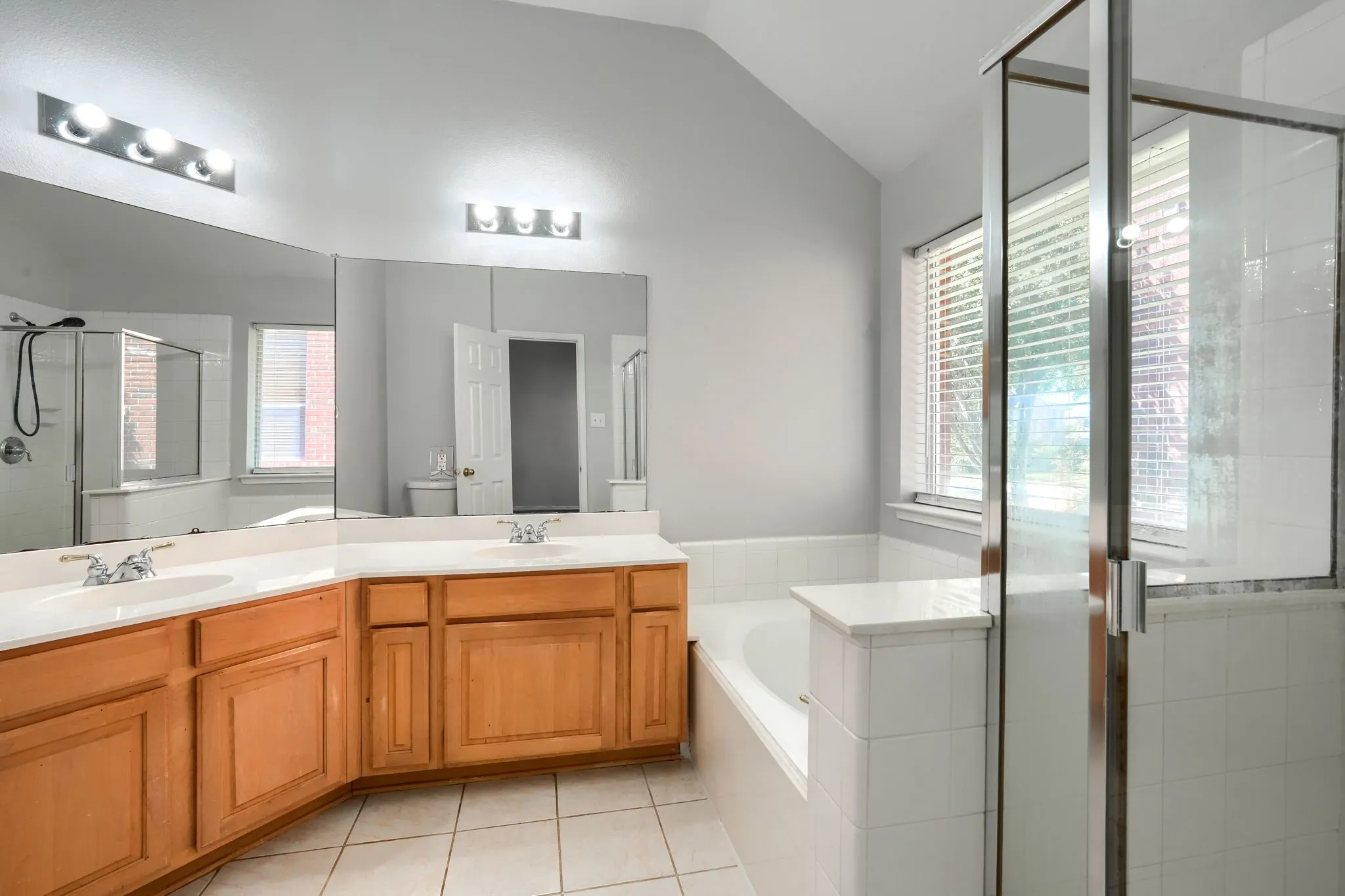 Bathroom featuring a corner vanity with dual sinks, light wood cabinetry, and a white countertop