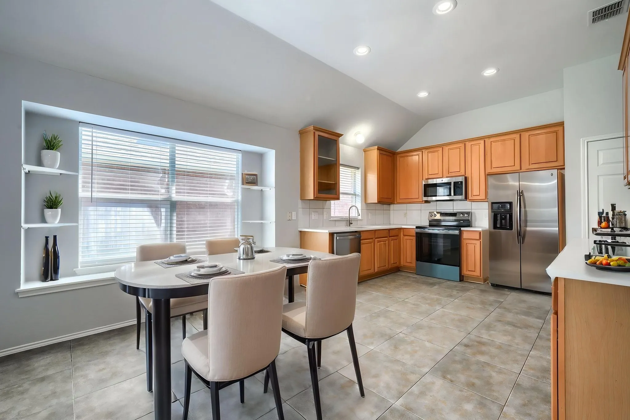 Open-concept kitchen and dining area featuring warm wood cabinetry, stainless steel appliances, recessed lighting, and tile flooring
