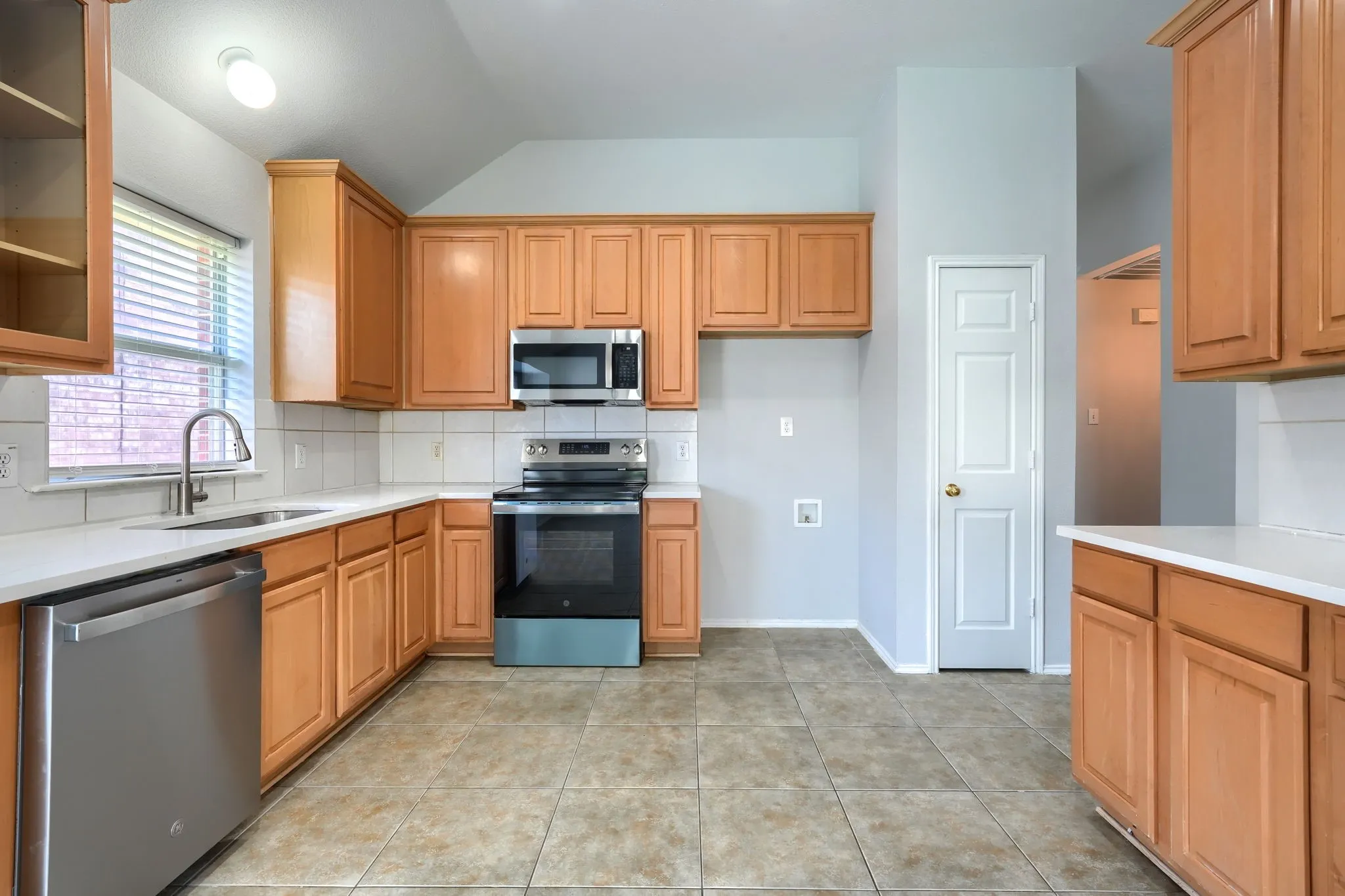 Kitchen featuring wood cabinetry, stainless steel appliances, white countertops, tile flooring, and a white tile backsplash