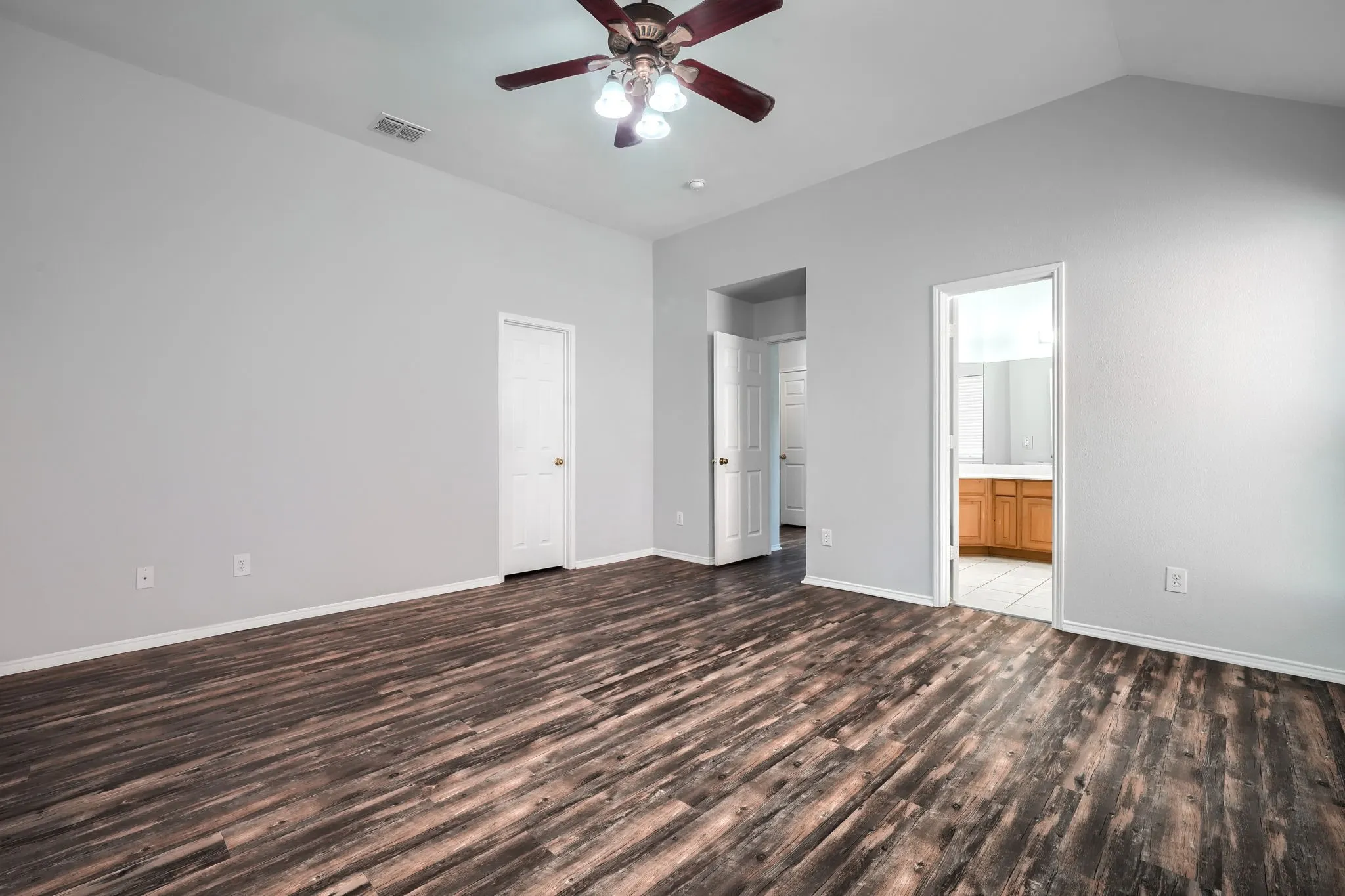 Spacious room featuring vaulted ceilings, a ceiling fan with integrated lighting, wood-finish flooring, and light-toned walls