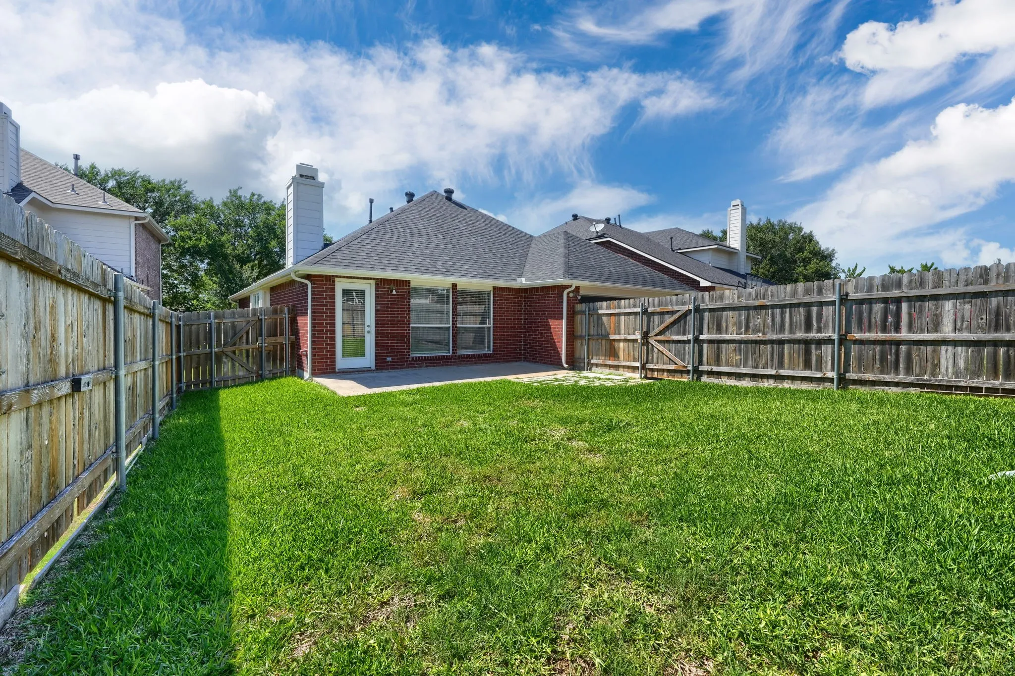 Spacious backyard featuring a manicured lawn, full perimeter privacy fencing, and a concrete patio