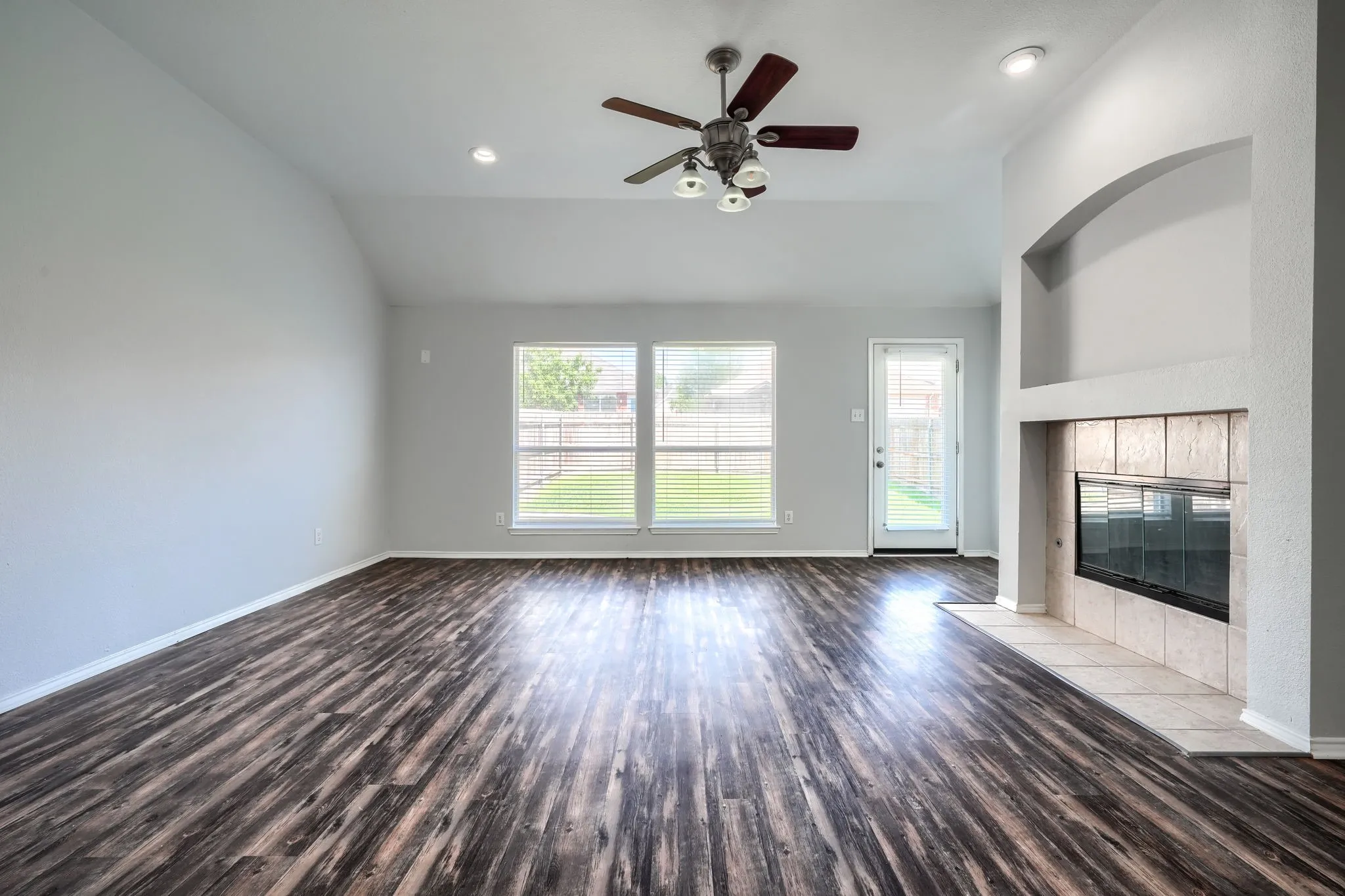 Spacious living area featuring wood-finish flooring, a tiled fireplace with an arched niche, and a ceiling fan