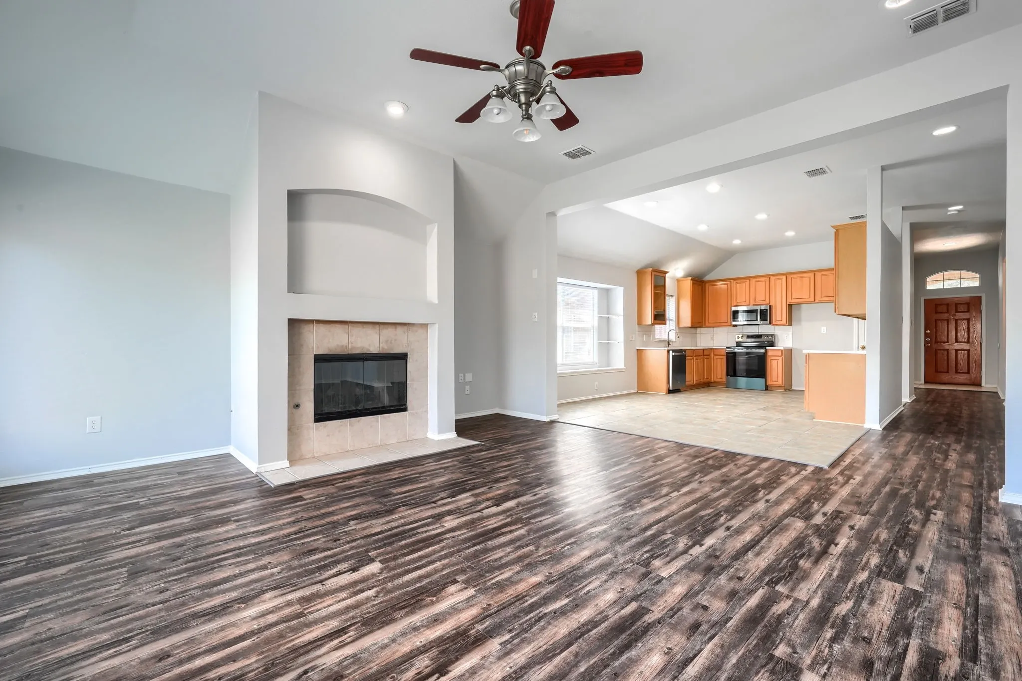 Spacious living area featuring wood-finish flooring, a built-in fireplace with a tiled surround, and an integrated arched niche