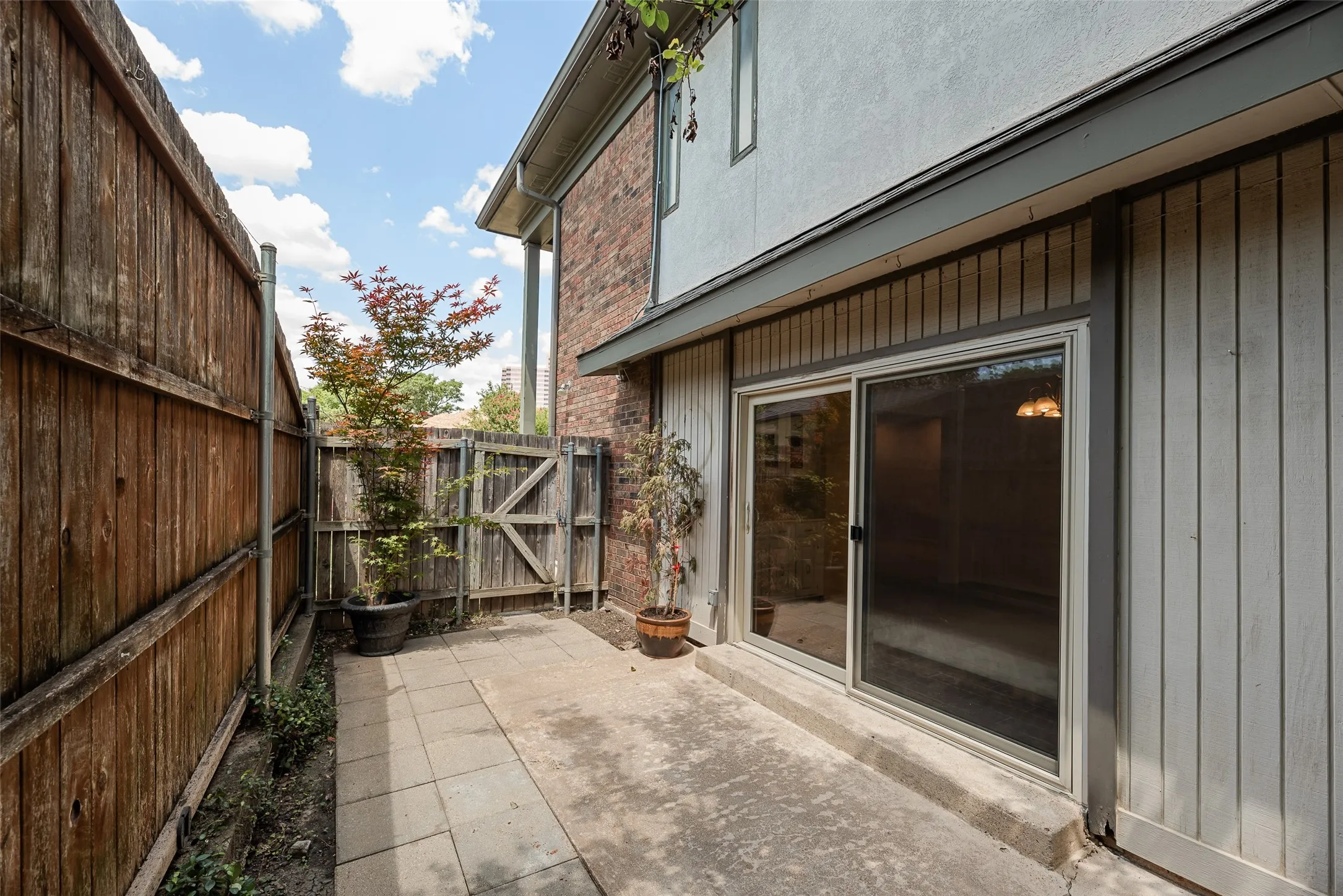 Private paved patio area featuring a wooden privacy fence, and sliding glass door access