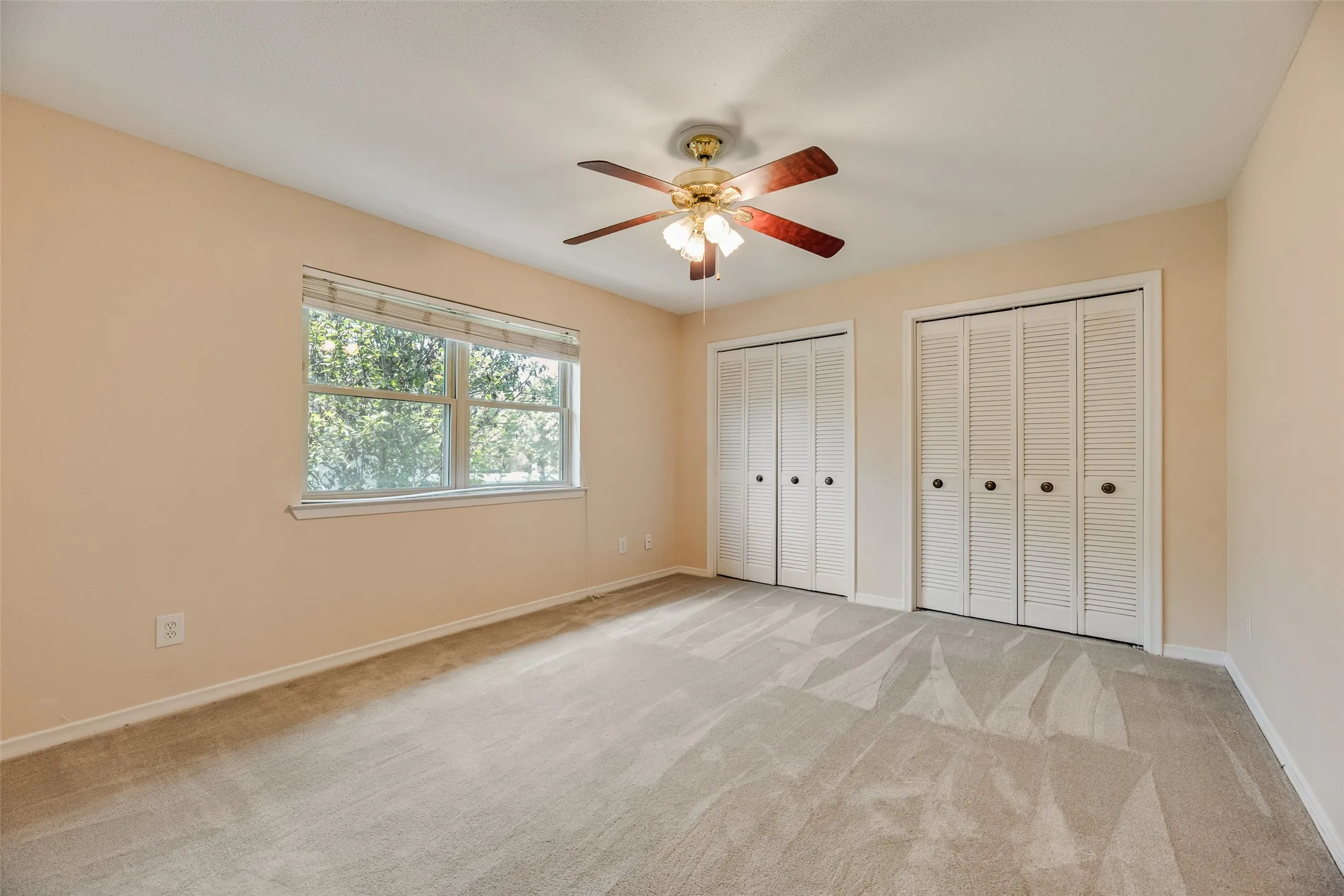 Bedroom featuring a window with blinds, two bi-fold closets, and a ceiling fan with light fixture