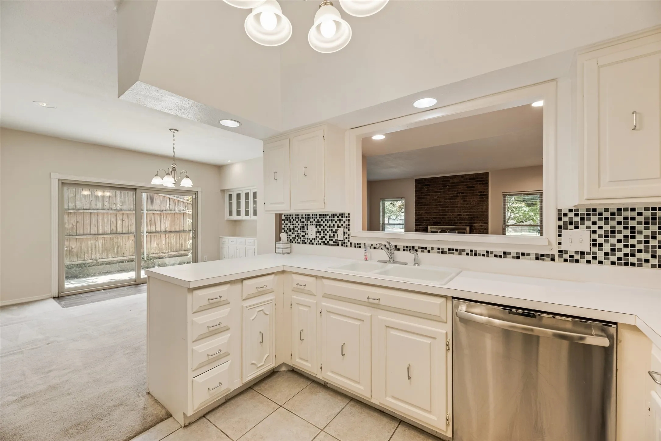 Kitchen featuring white cabinetry, solid surface countertops, tile backsplash, stainless steel dishwasher, and a pass-through window